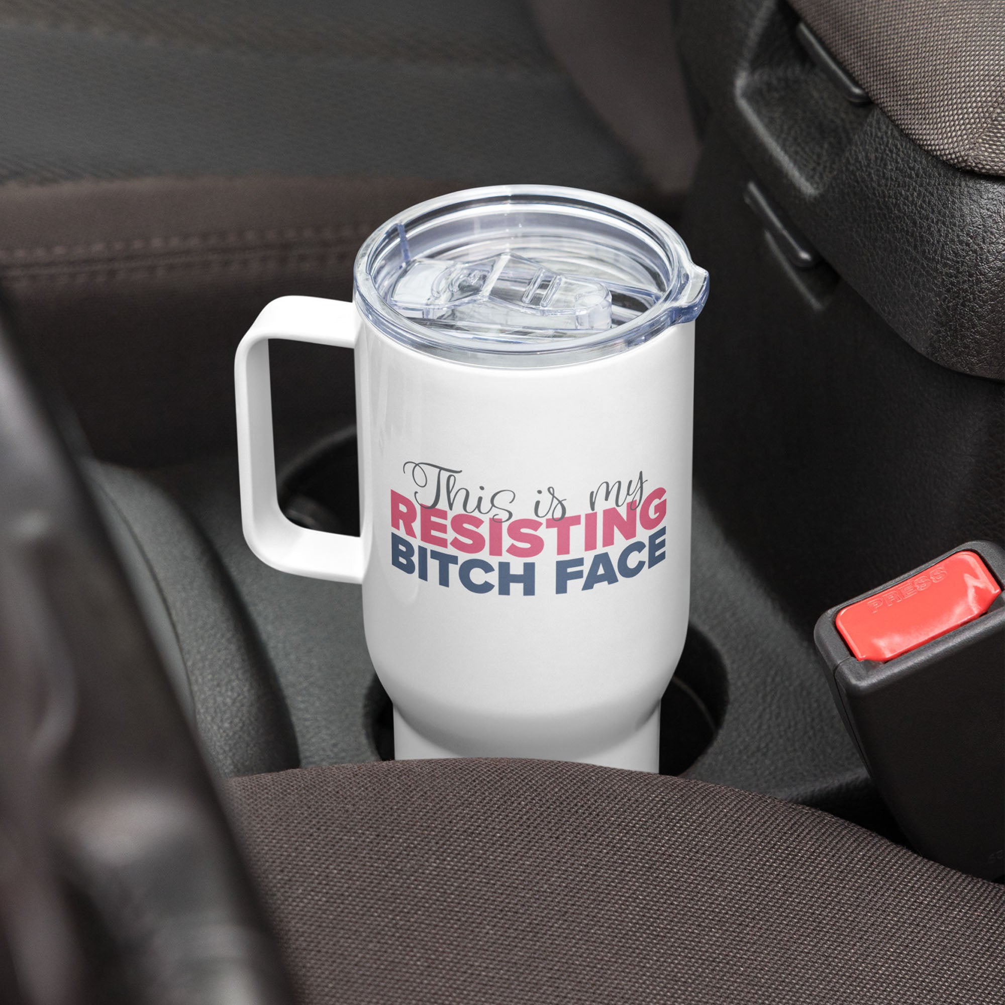 25 ounce white insulated travel tumbler with the phrase “This Is My Resisting Bitch Face” printed in script and bold text, in a car cup holder.