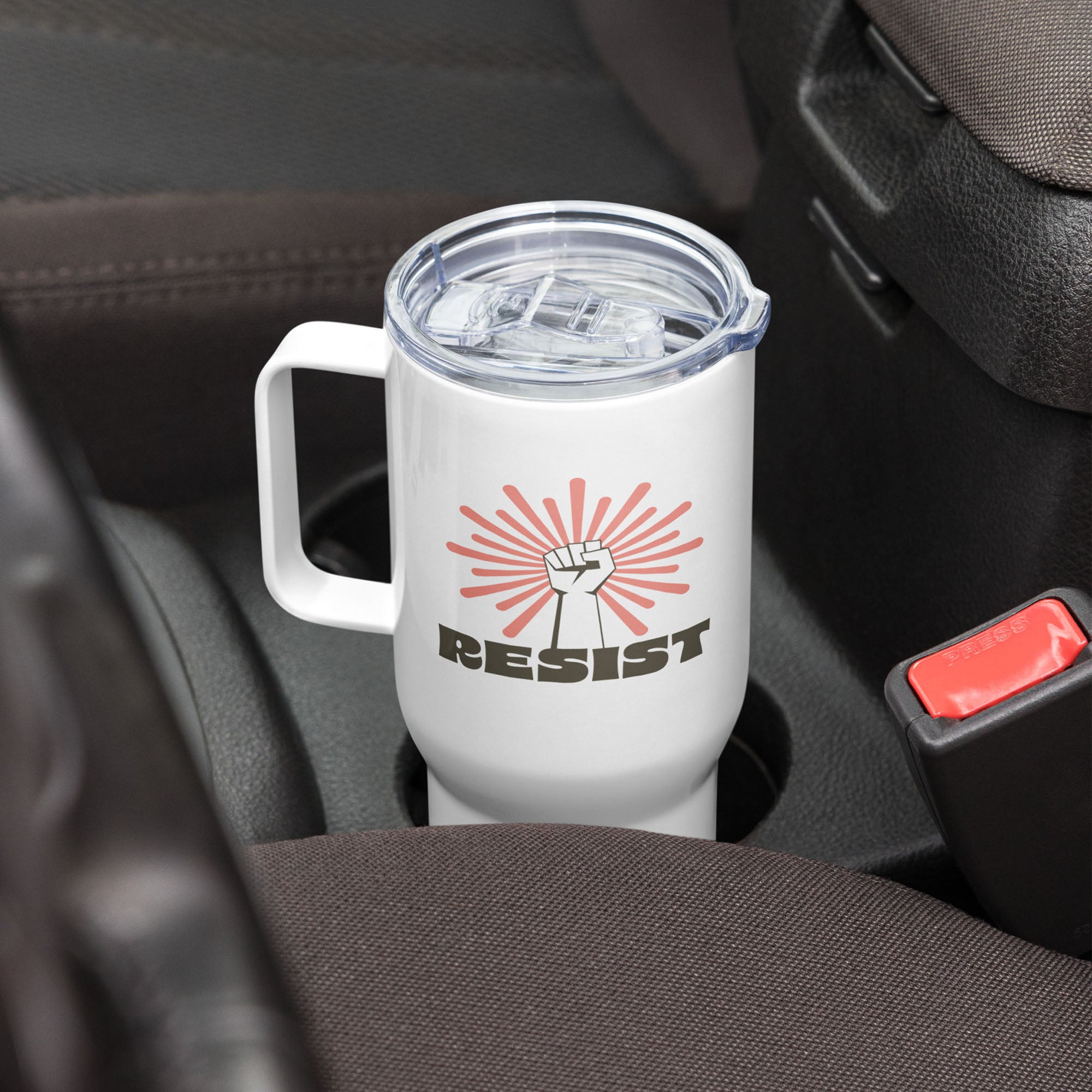 25 ounce white stainless steel tumbler with handle, with graphic text "resist" below a raised fist and coral color burst, in a car cup holder.