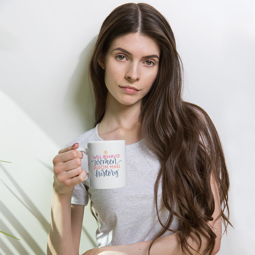 Woman holding a mug with text that reads "well-behaved women seldom make history" against a plain background