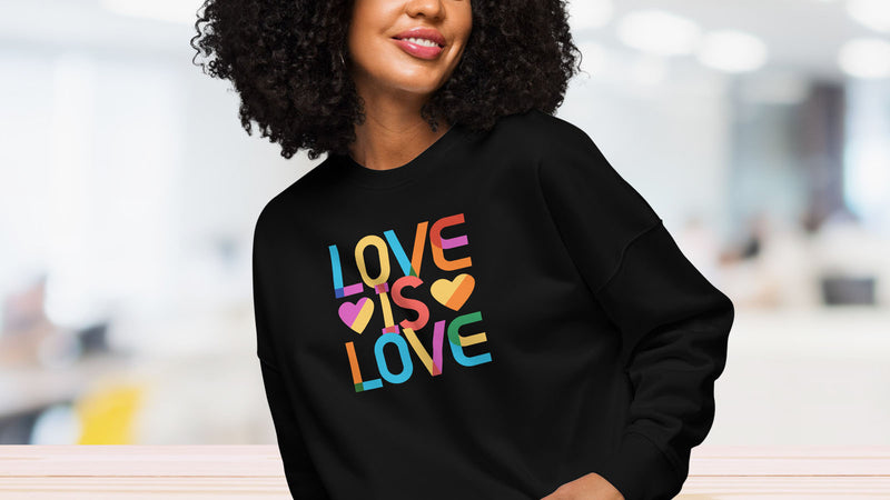 Female model wearing navy sweatshirt with rainbow text that reads "love is love."