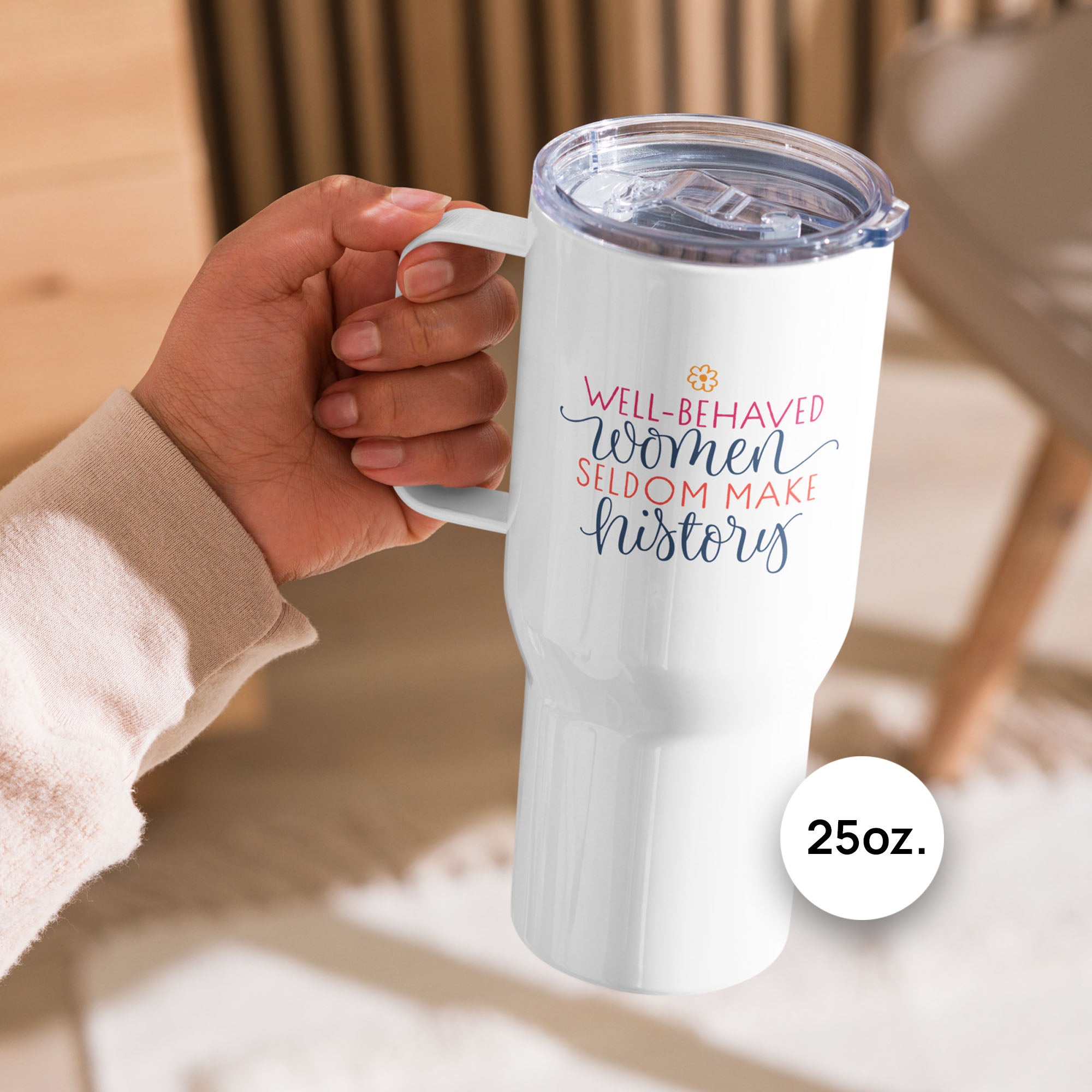 Person holding 25 ounce white insulated travel tumblers with handle featuring the quote “Well-Behaved Women Seldom Make History” in colorful stylized text block, on an outdoor deck.