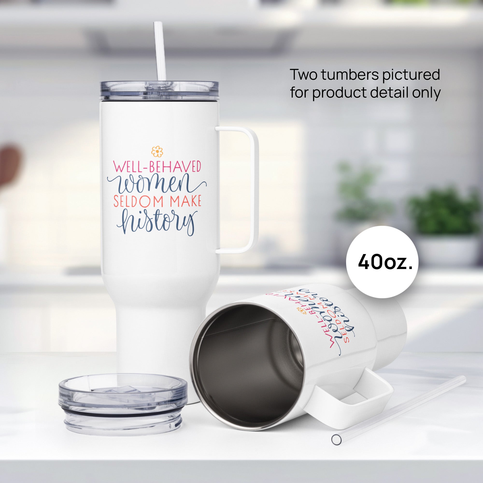 Two 40 ounce white insulated travel tumblers with handle featuring the quote “Well-Behaved Women Seldom Make History” in colorful stylized text block, sitting on kitchen countertop, one on its side with lid off.