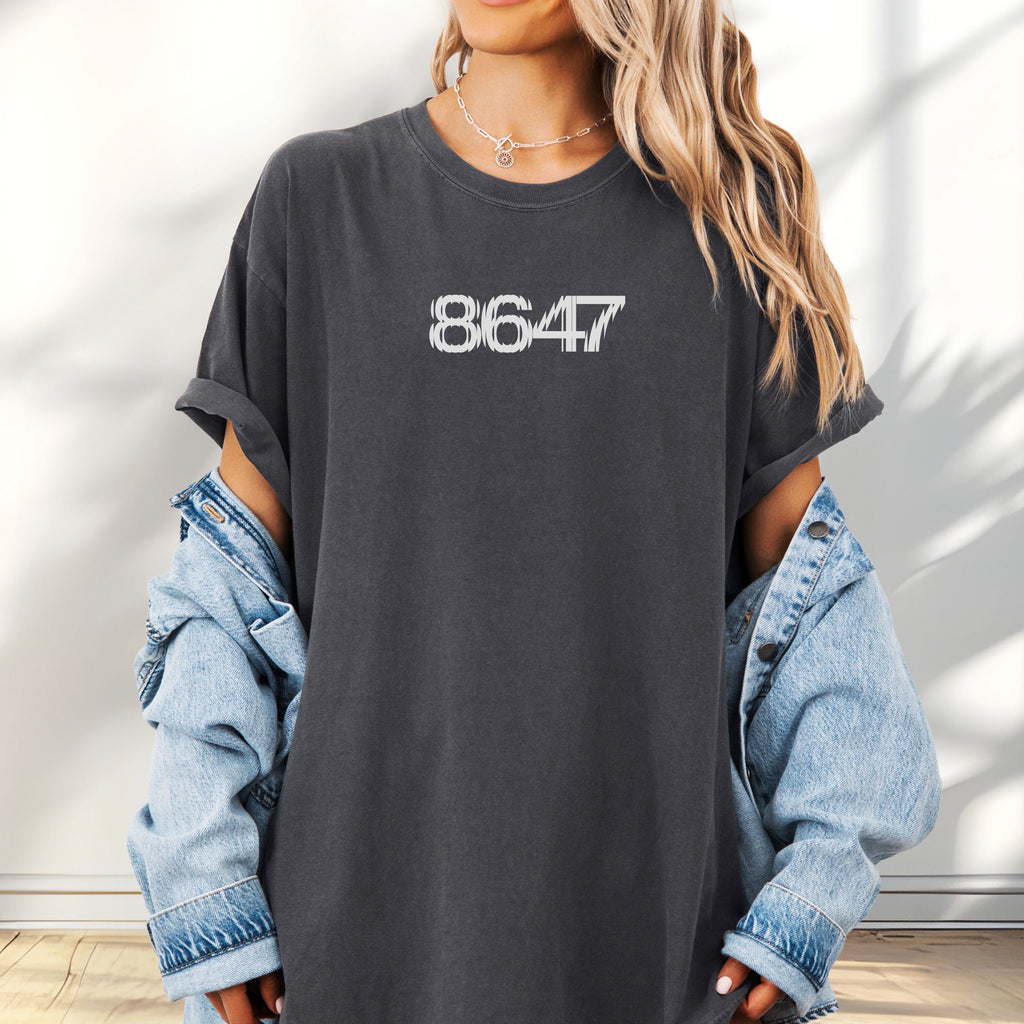 Feale model wearing oversized pepper t-shirt featuring the number “8647” in bold, clean typography with glass block effect.