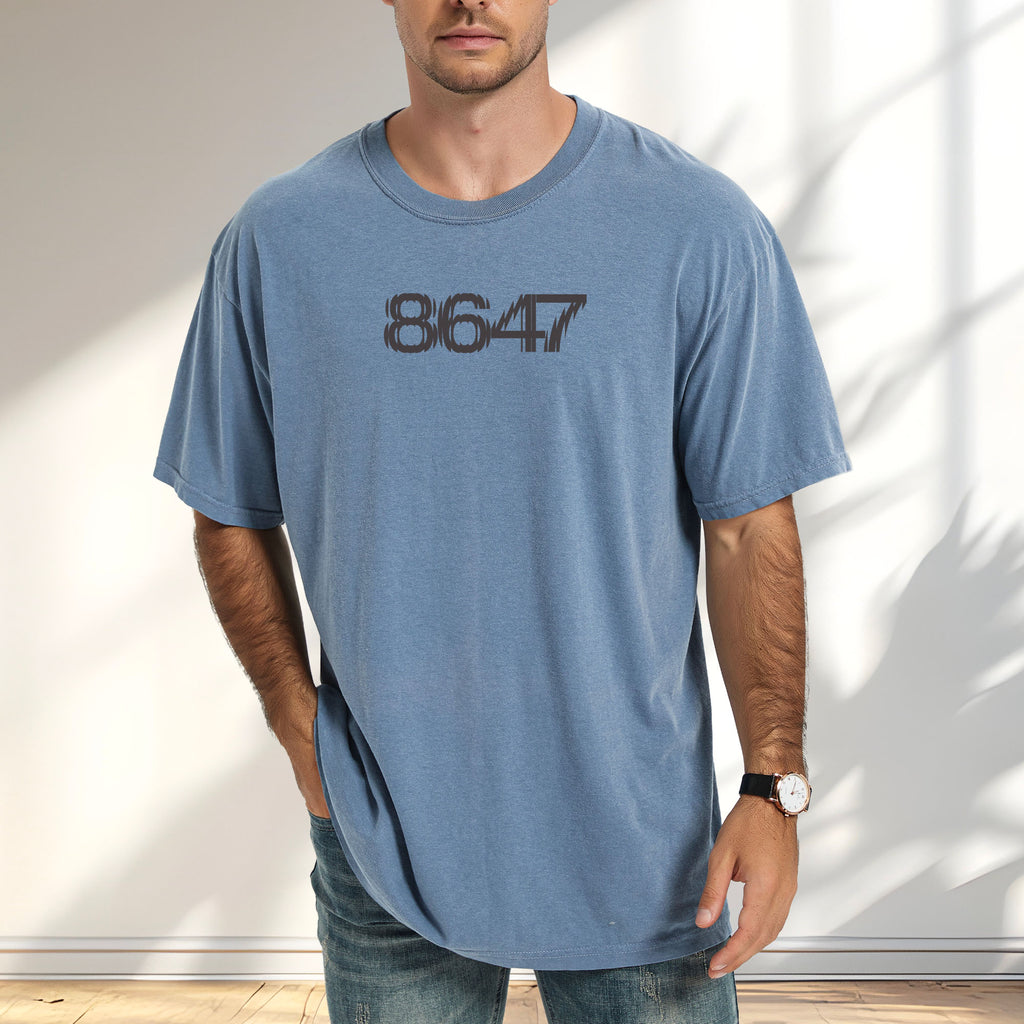 Male model wearing blue jean unisex t-shirt featuring the number “8647” in bold, clean typography with glass block effect, referencing Trump impeachment.