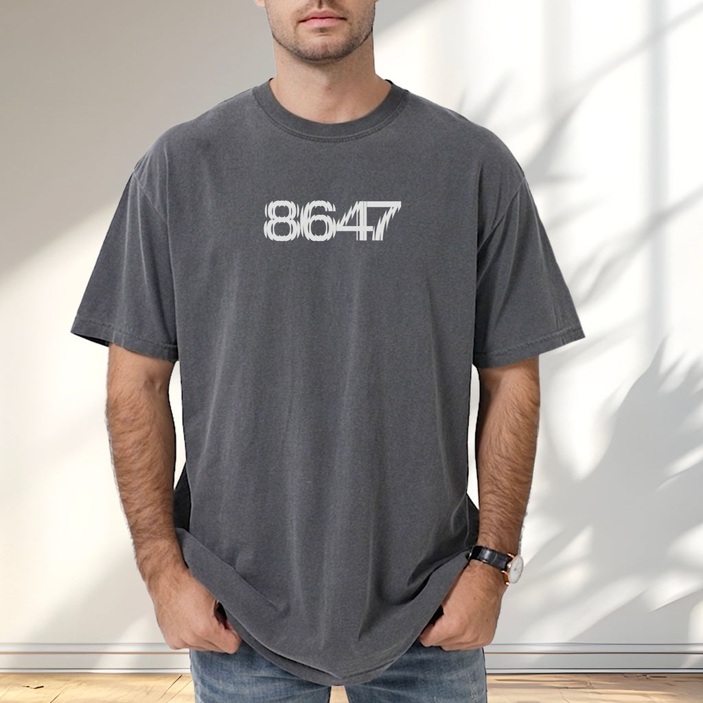 Male model wearing pepper unisex t-shirt featuring the number “8647” in bold, clean typography with glass block effect, referencing Trump impeachment.