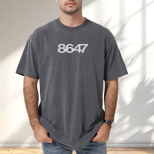 Male model wearing pepper unisex t-shirt featuring the number “8647” in bold, clean typography with glass block effect, referencing Trump impeachment.