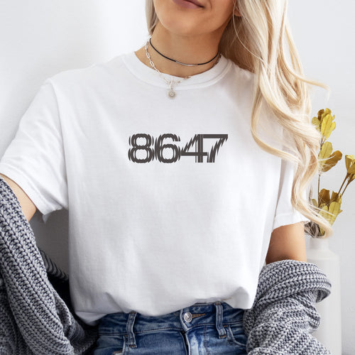 Female model wearing white unisex t-shirt featuring the number “8647” in bold, clean typography with glass block effect, referencing Trump impeachment.