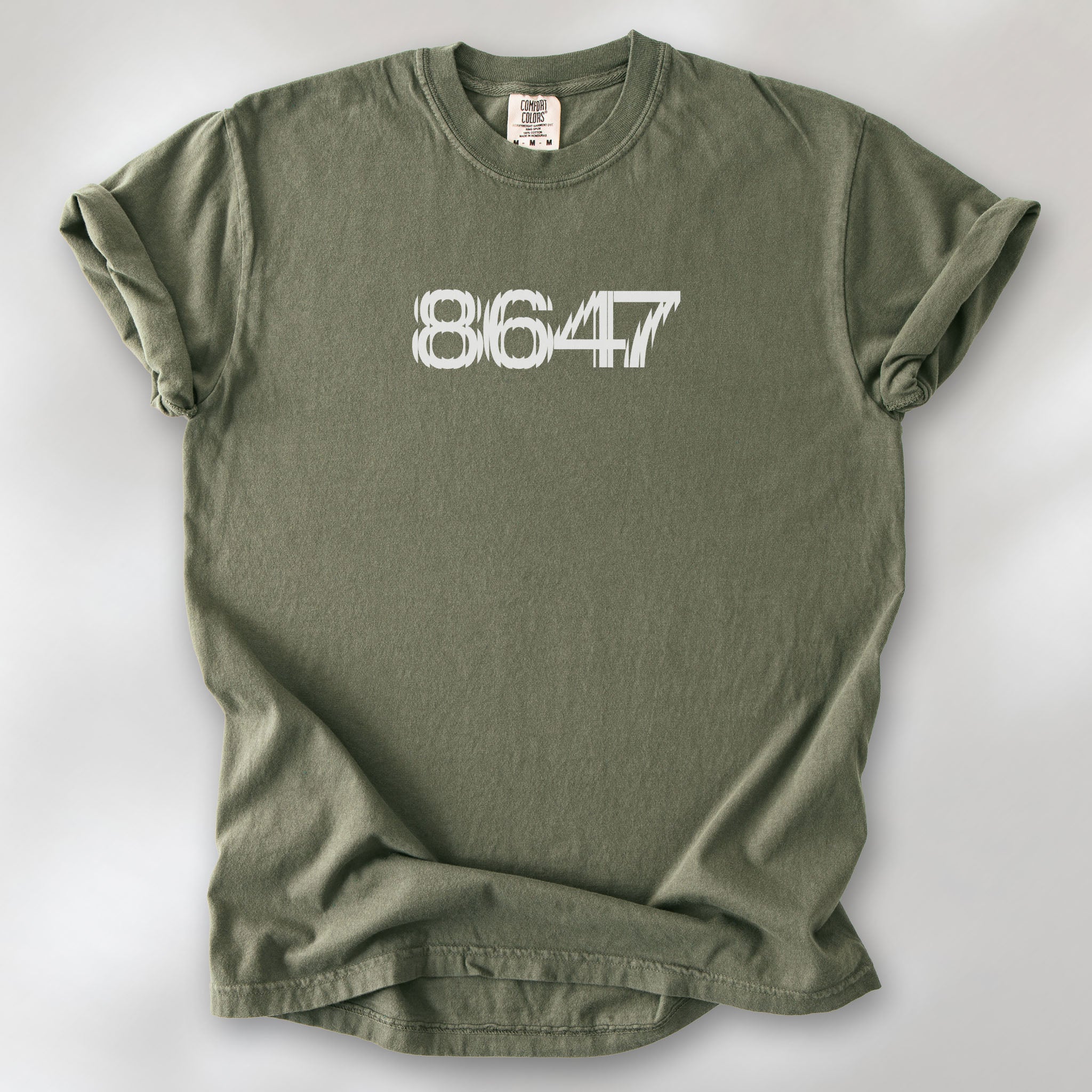 Sage unisex t-shirt featuring the number “8647” in bold, clean typography with glass block effect, referencing Trump impeachment.