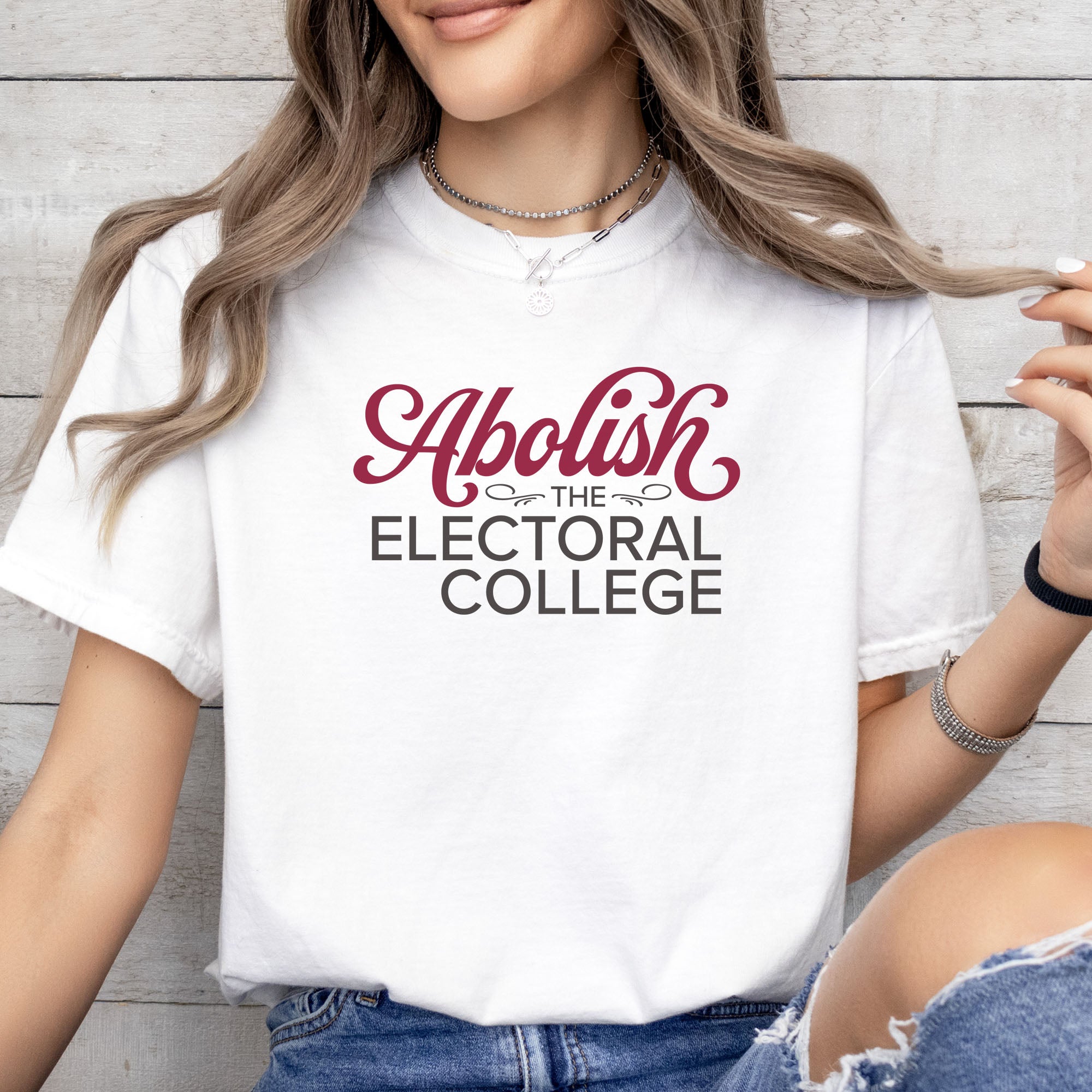 Female model wearing white t-shirt with stylized text reading “Abolish the Electoral College” in muted red and gray.