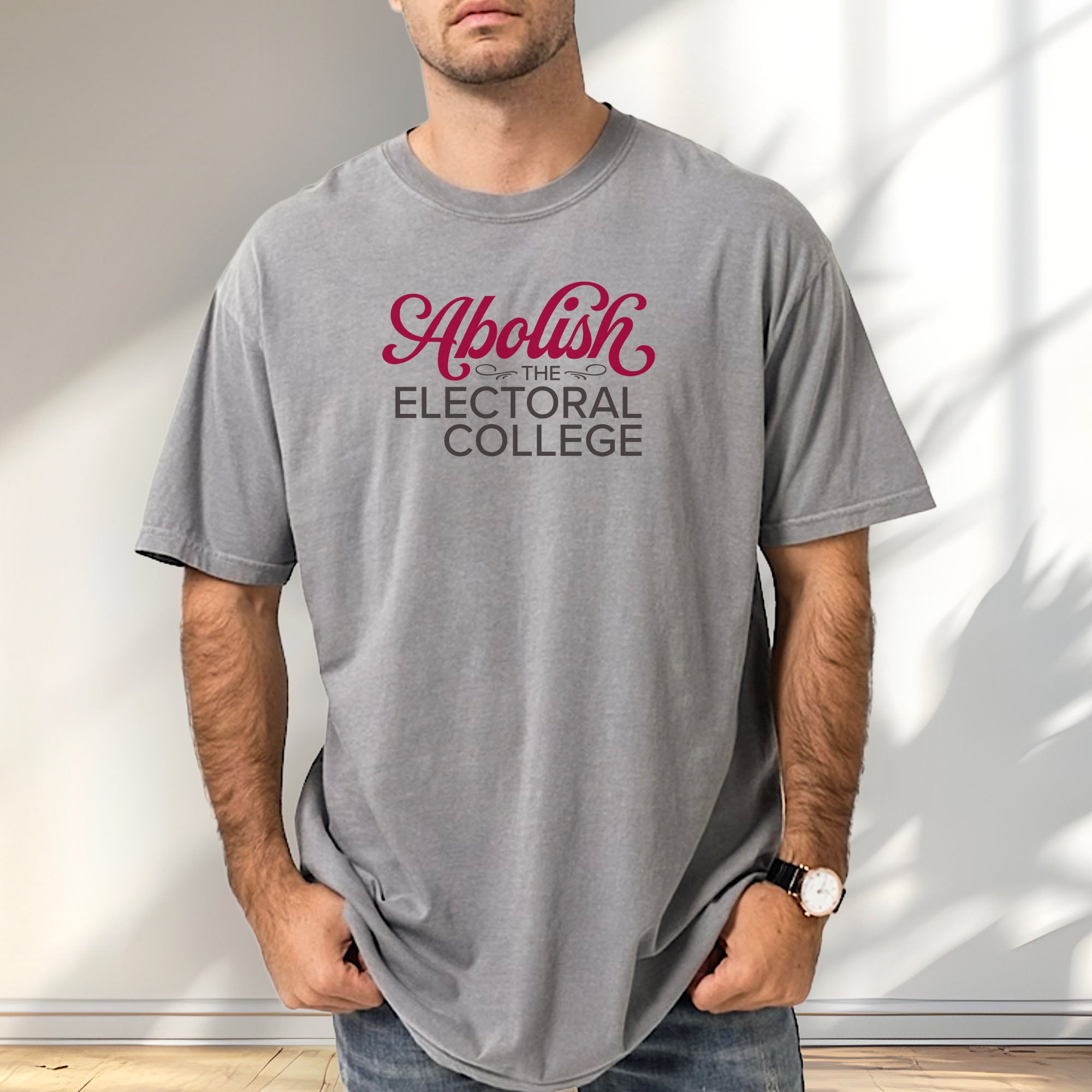 Male model wearing grey t-shirt with stylized text reading “Abolish the Electoral College” in muted red and gray.