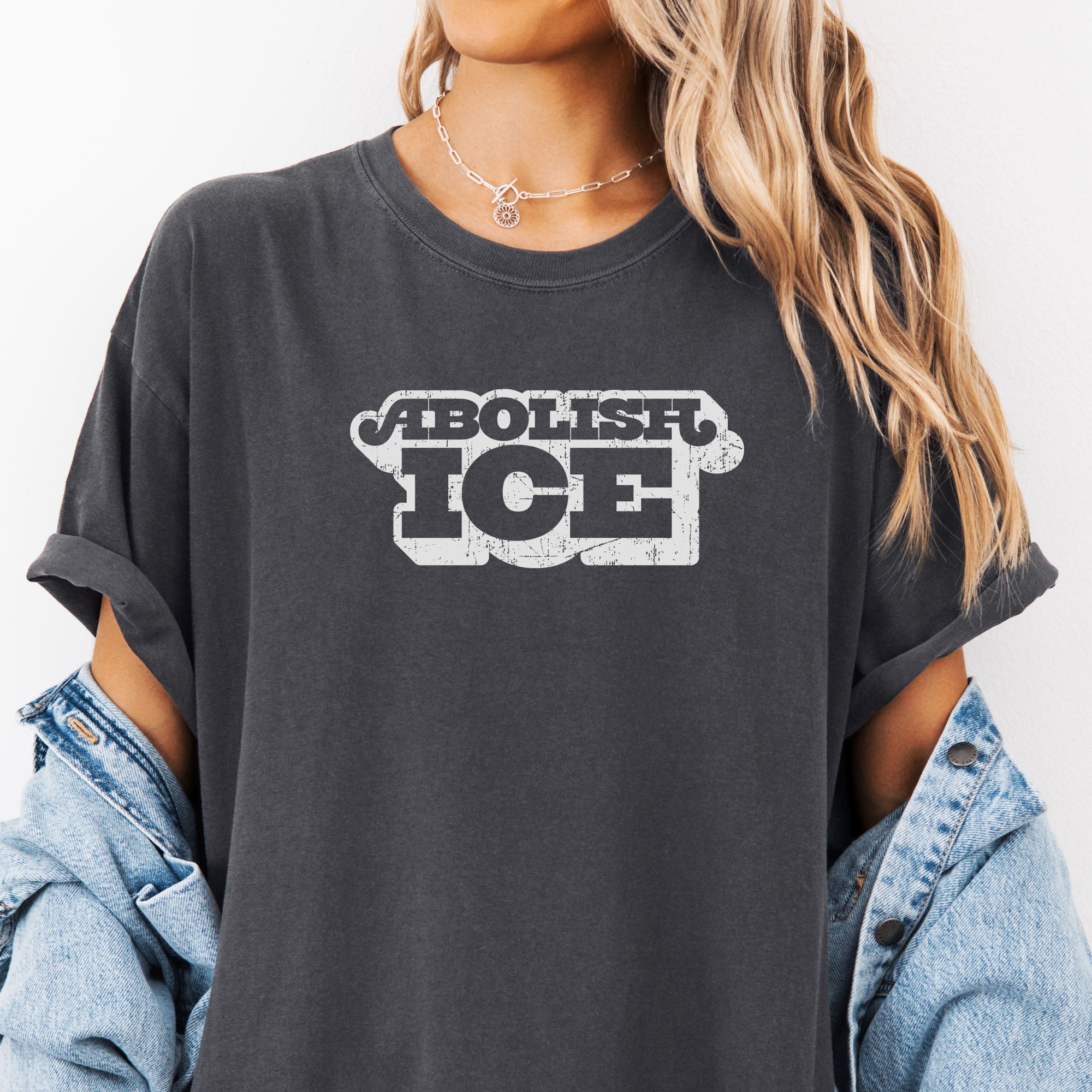 Female model wearing oversized pepper t-shirt with retro distressed text reading “Abolish ICE” for immigration justice and anti-ICE activism.