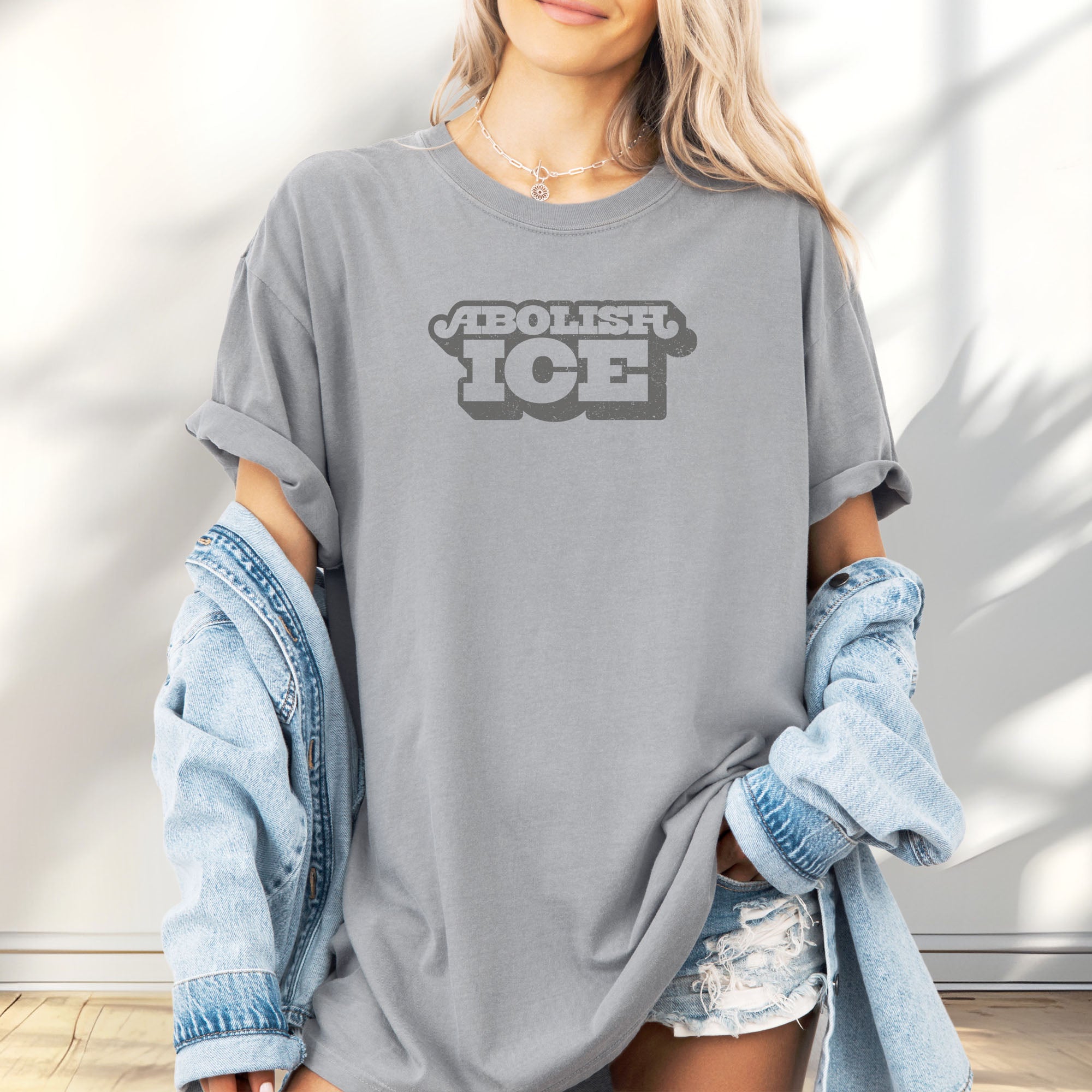Female model wearing graphite t-shirt with retro text reading “Abolish ICE” for immigration justice and anti-ICE activism.