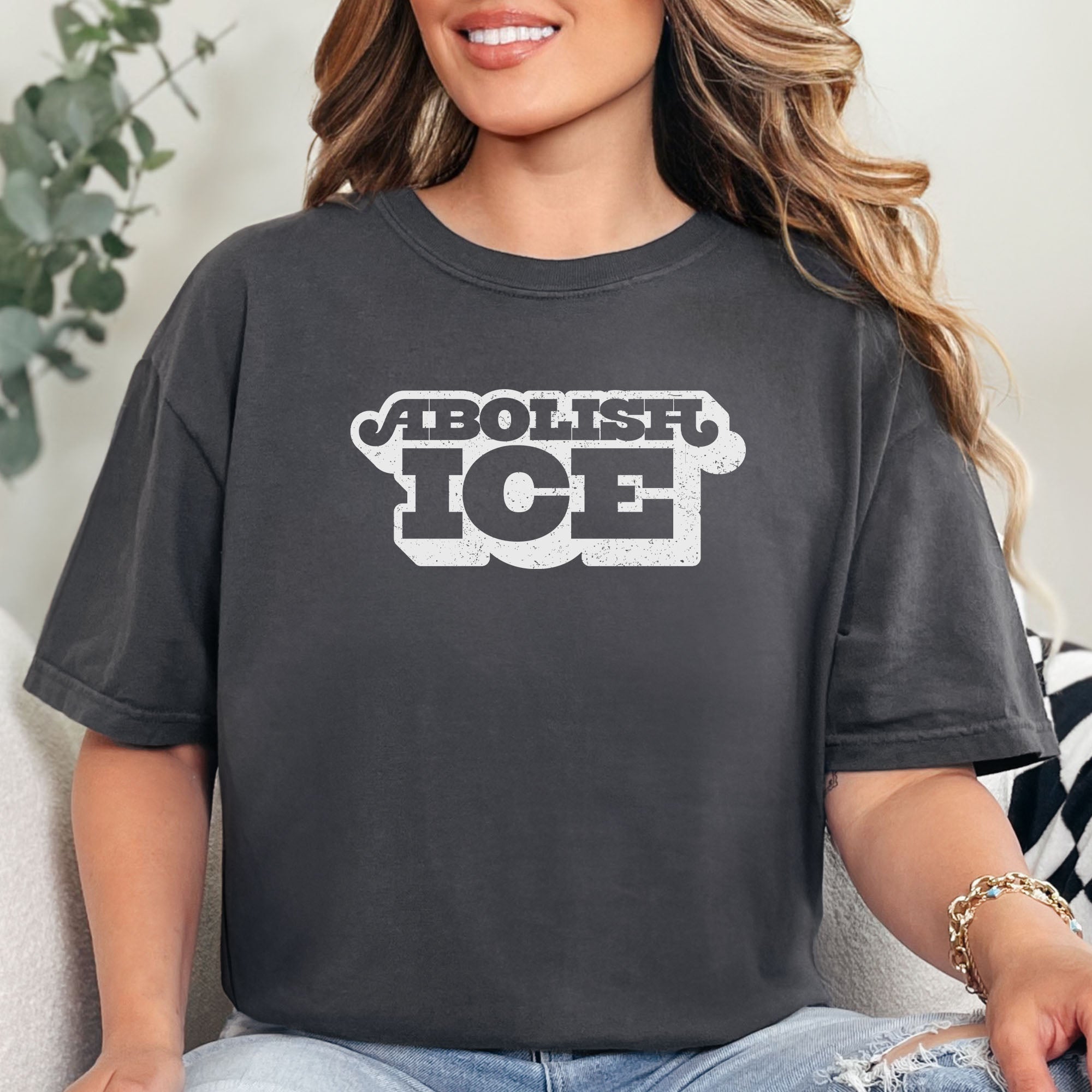 Female model wearing graphite t-shirt with retro text reading “Abolish ICE” for immigration justice and anti-ICE activism.