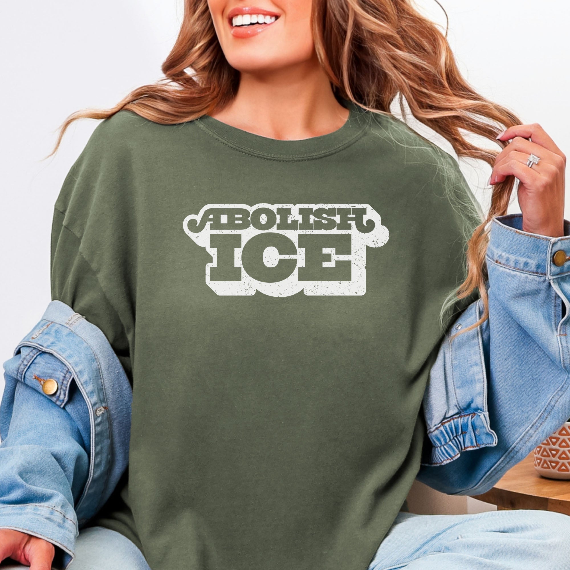Female model wearing sage t-shirt with retro text reading “Abolish ICE” for immigration justice and anti-ICE activism.