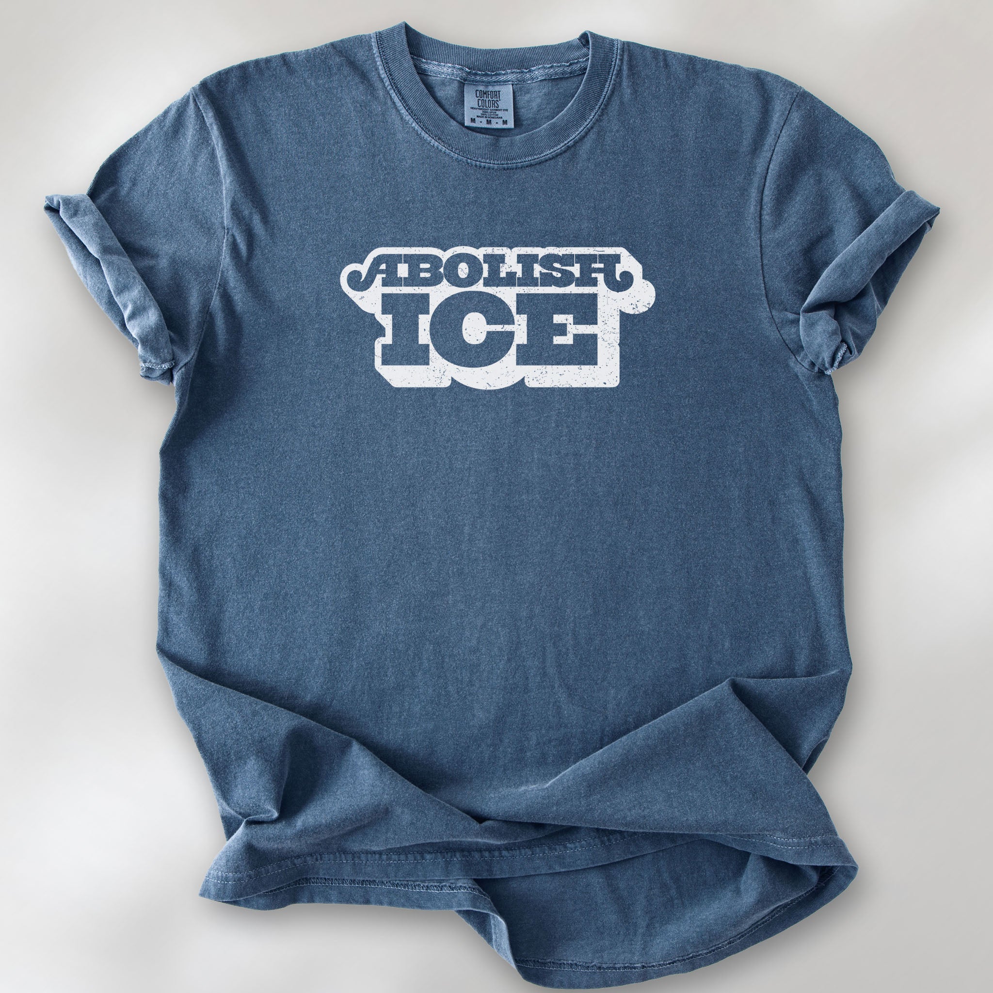 Denim t-shirt with retro text reading “Abolish ICE” for immigration justice and anti-ICE activism.