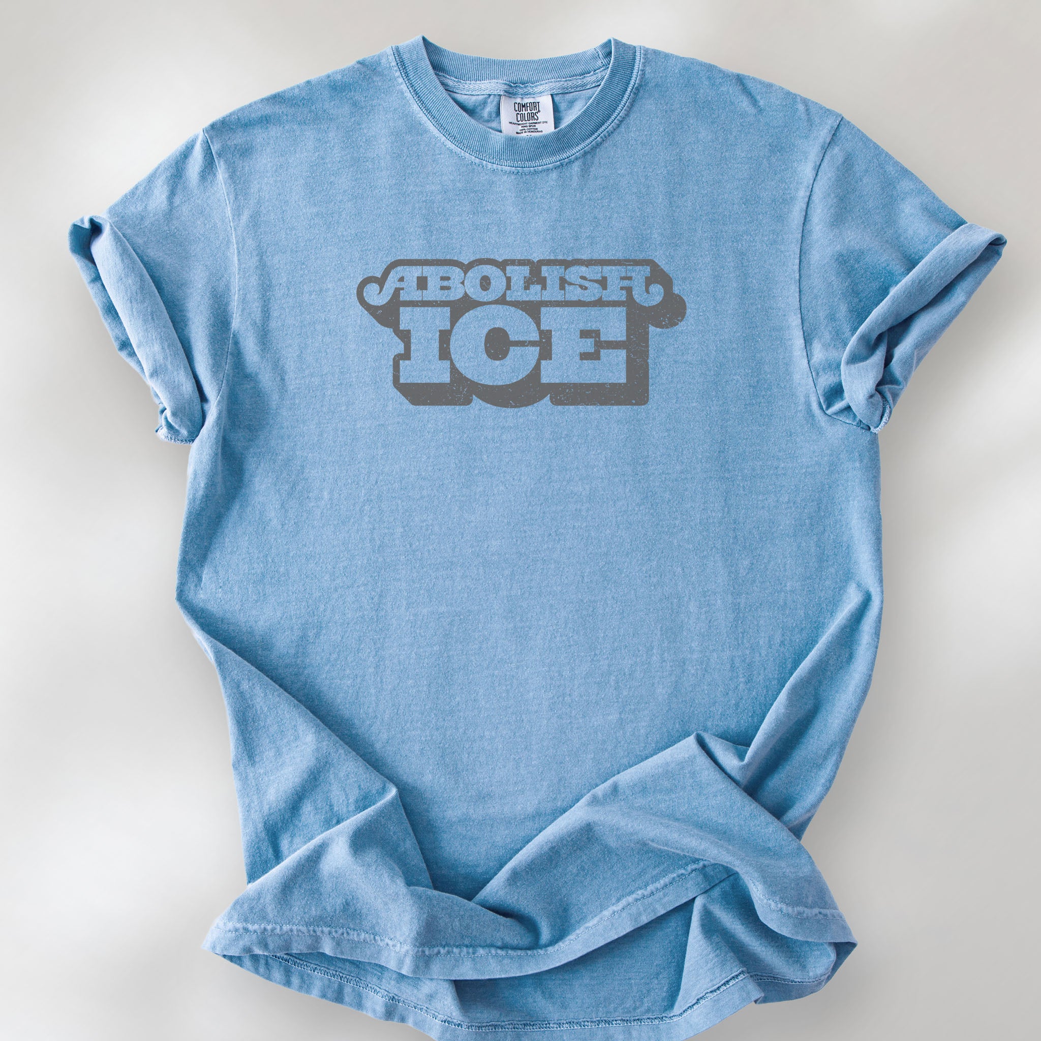 Washed denim t-shirt with retro text reading “Abolish ICE” for immigration justice and anti-ICE activism.