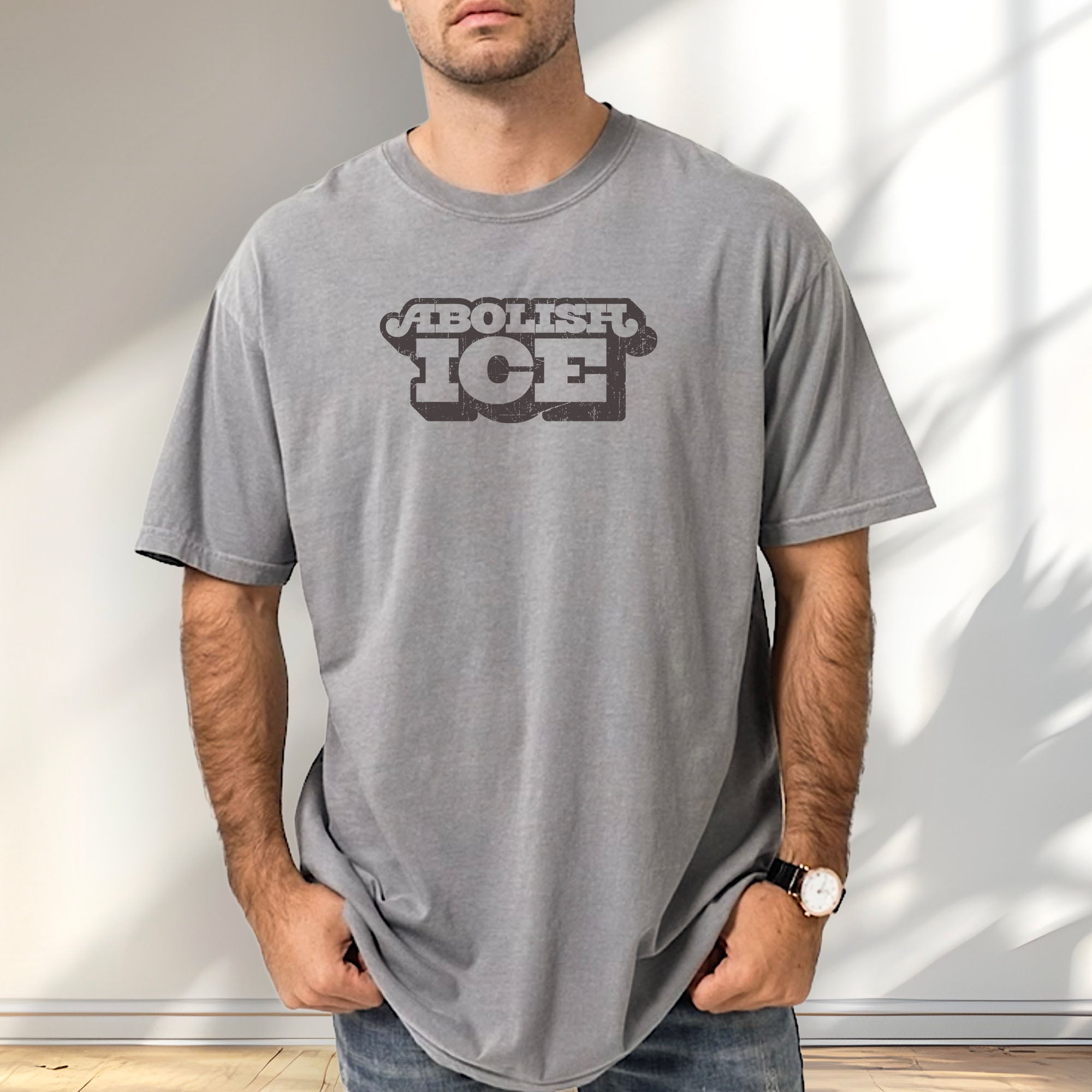 Male model wearing grey t-shirt with retro distressed text reading “Abolish ICE” for immigration justice and anti-ICE activism.
