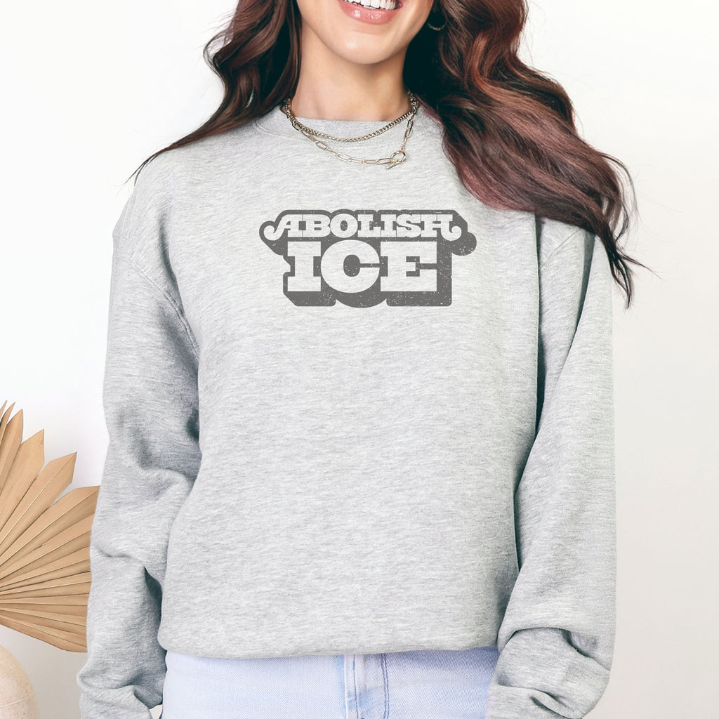 Female model wearing grey sweatshirt with retro text reading “Abolish ICE” for immigration justice and anti-ICE activism.