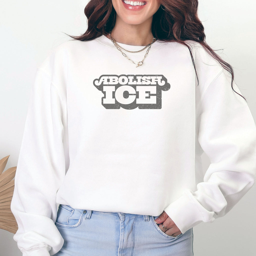 Female model wearing white sweatshirt with retro text reading “Abolish ICE” for immigration justice and anti-ICE activism.
