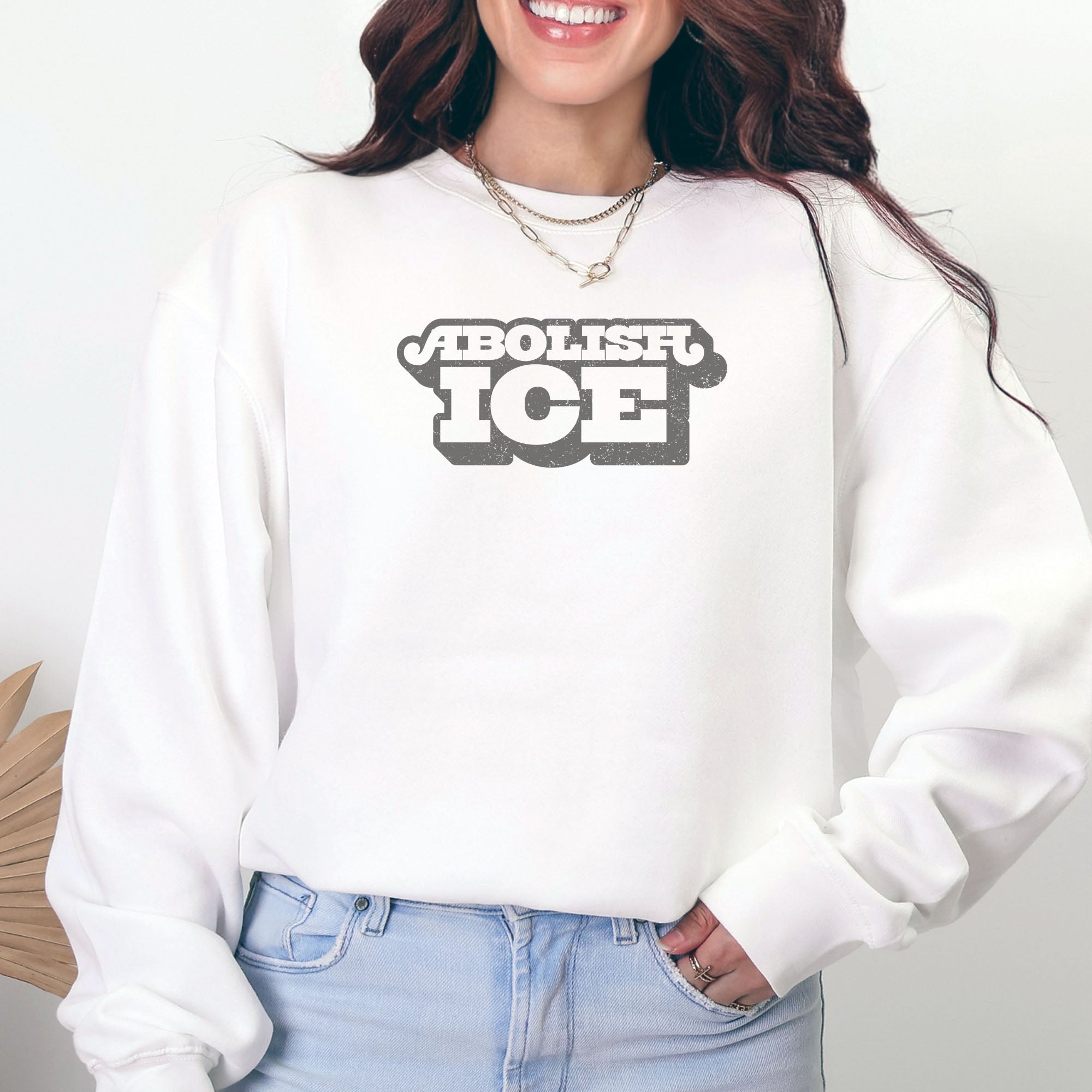 Female model wearing white sweatshirt with retro text reading “Abolish ICE” for immigration justice and anti-ICE activism.