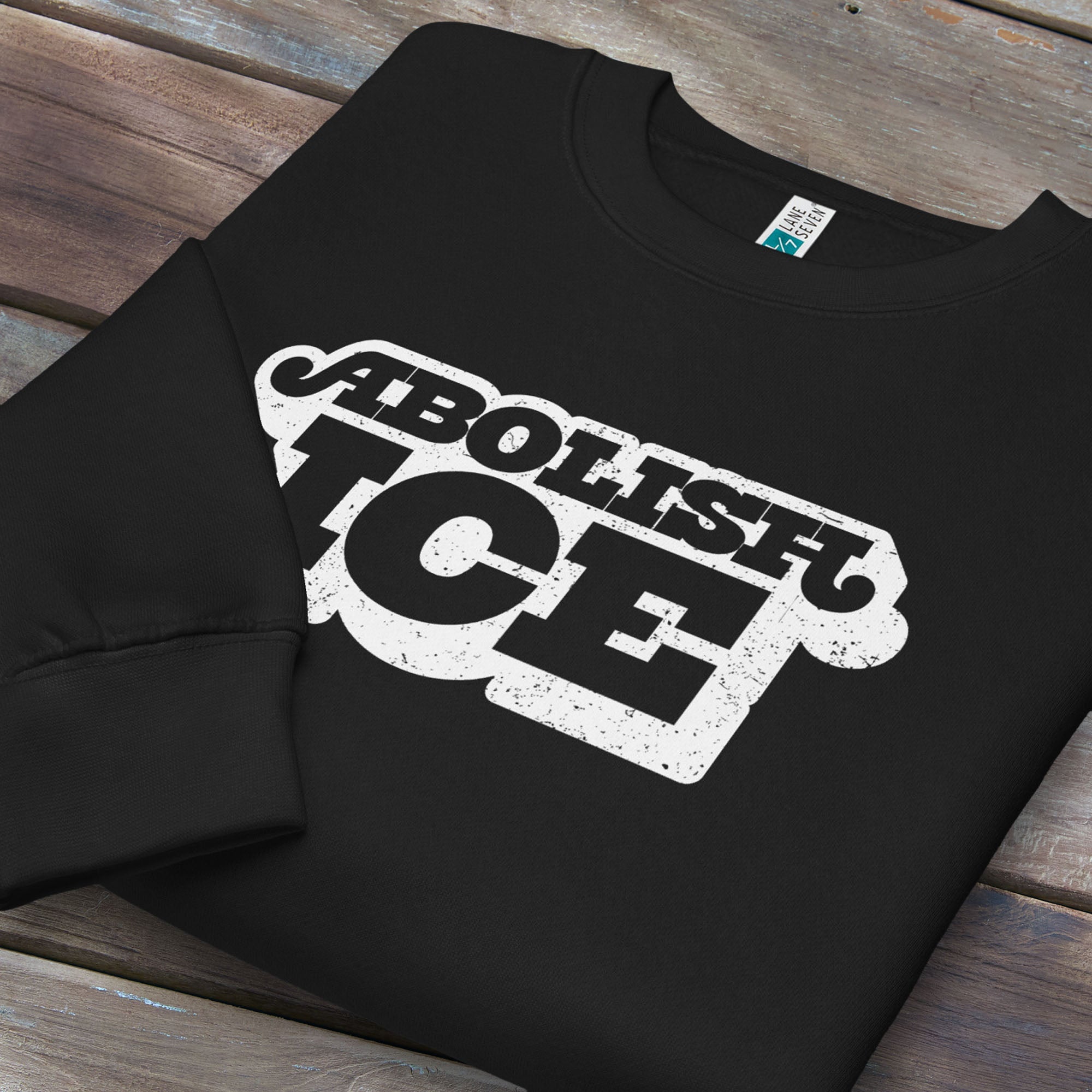 Folded black sweatshirt with retro text reading “Abolish ICE” for immigration justice and anti-ICE activism.