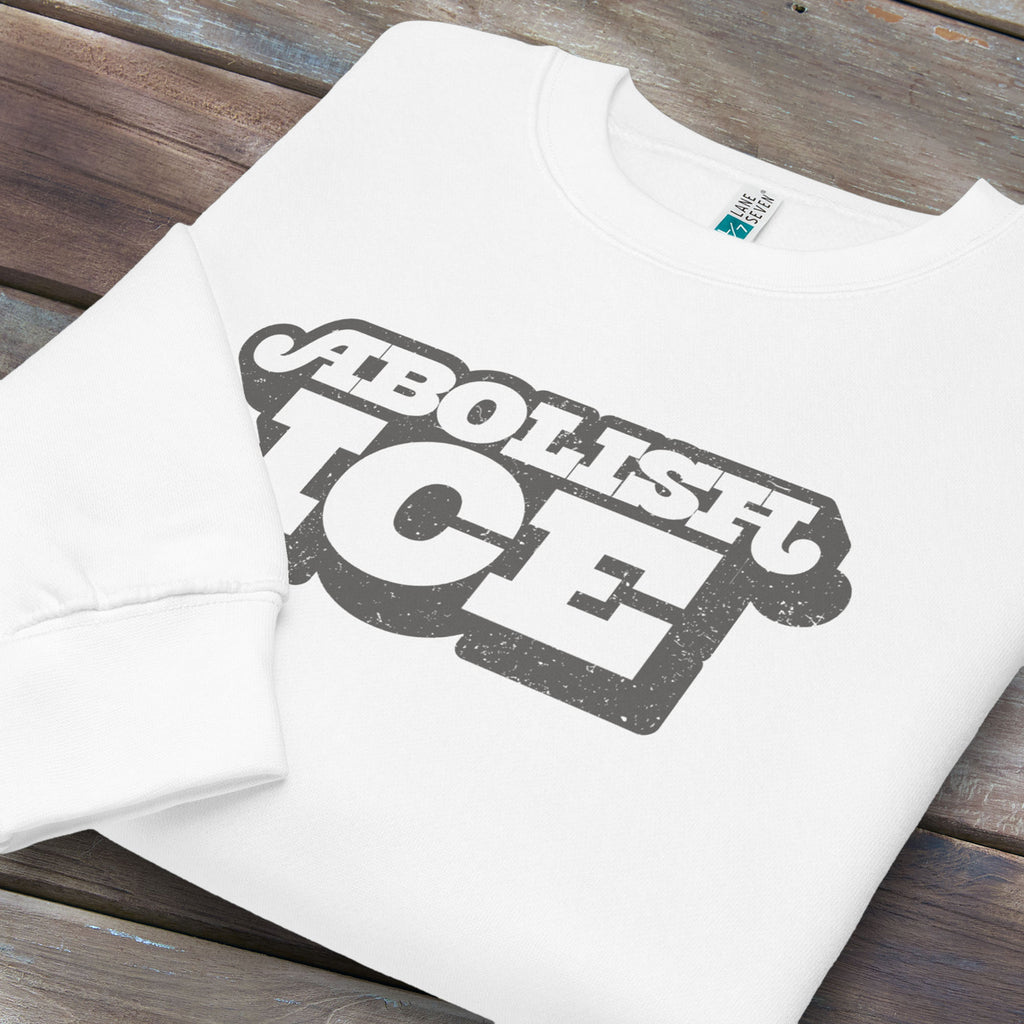 Folded white sweatshirt with retro text reading “Abolish ICE” for immigration justice and anti-ICE activism.
