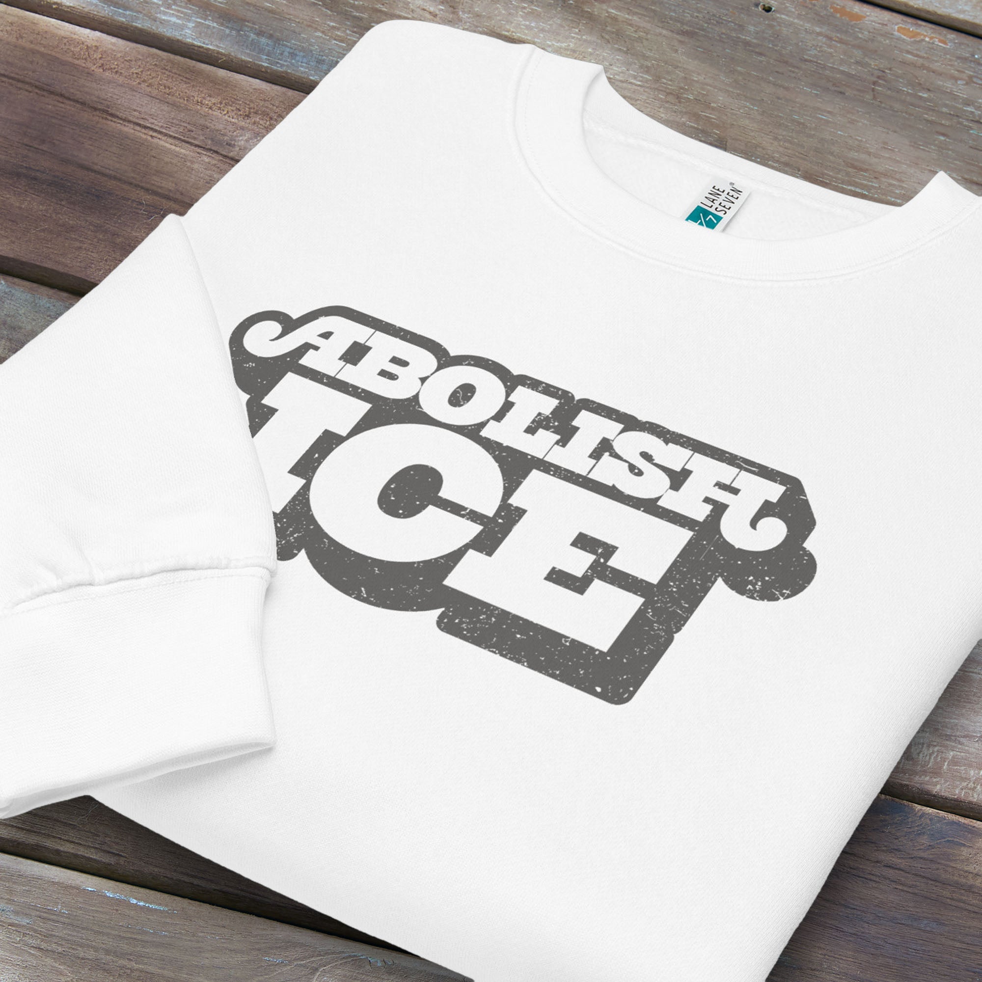 Folded white sweatshirt with retro text reading “Abolish ICE” for immigration justice and anti-ICE activism.