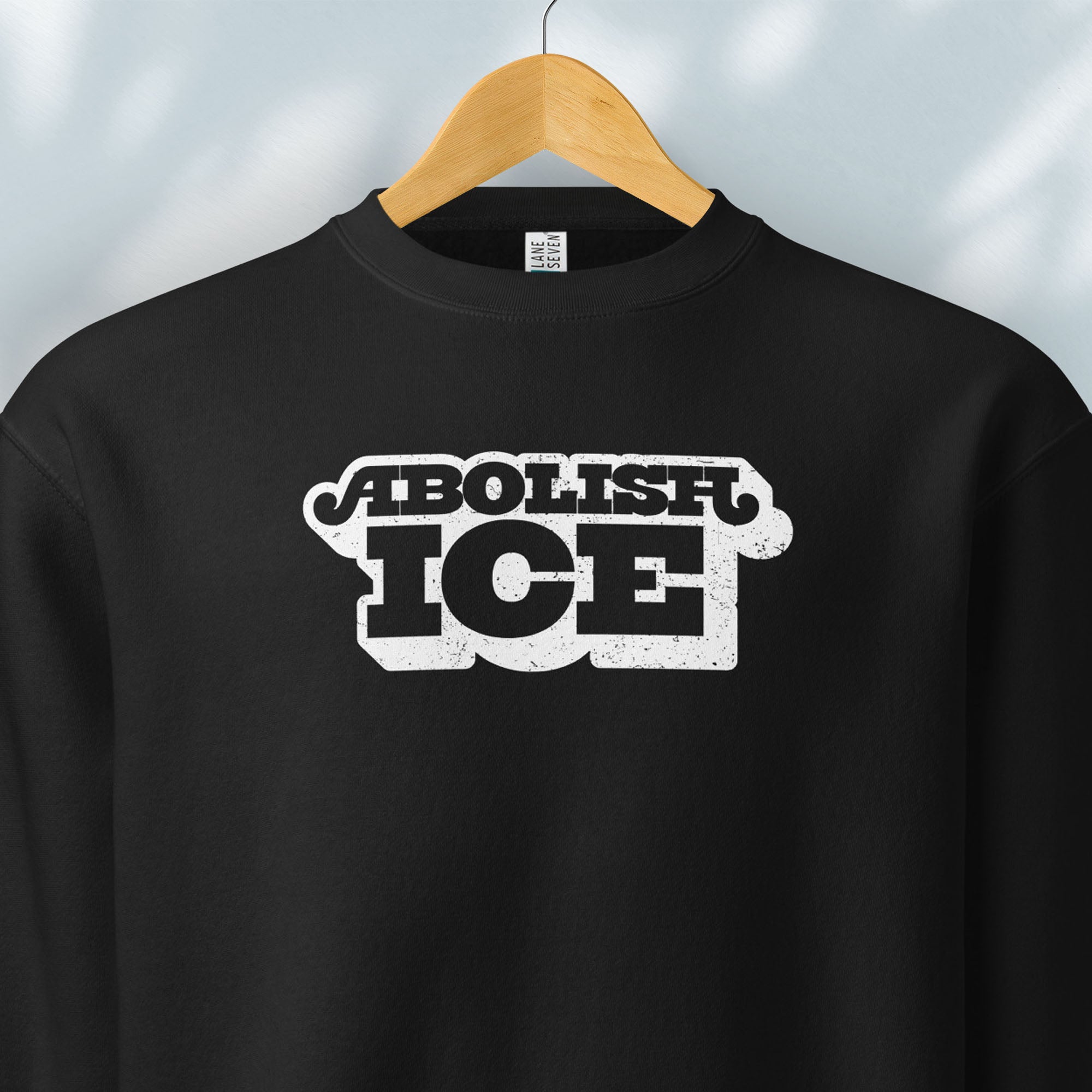 Hanging black sweatshirt with retro text reading “Abolish ICE” for immigration justice and anti-ICE activism.