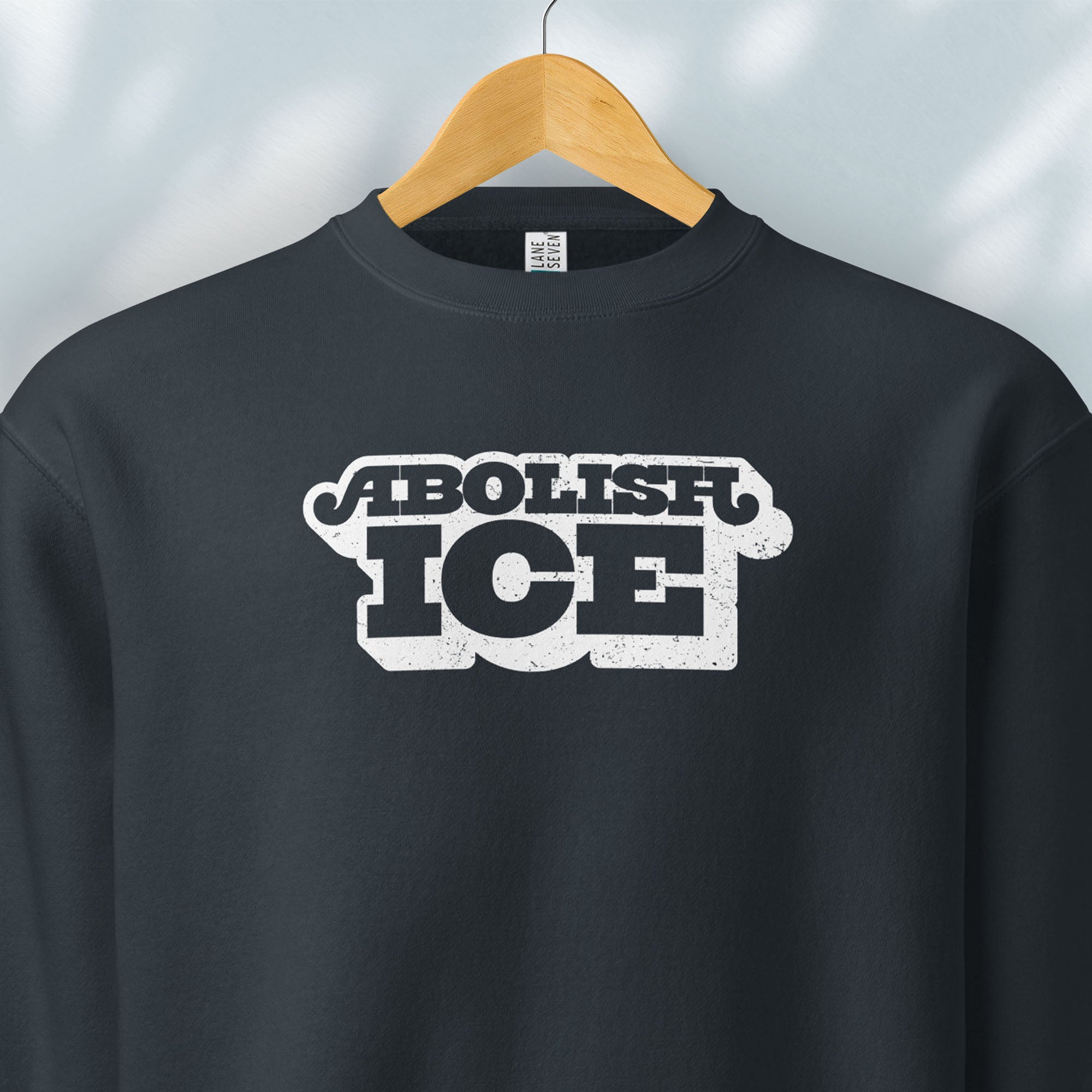 Hanging navy sweatshirt with retro text reading “Abolish ICE” for immigration justice and anti-ICE activism.