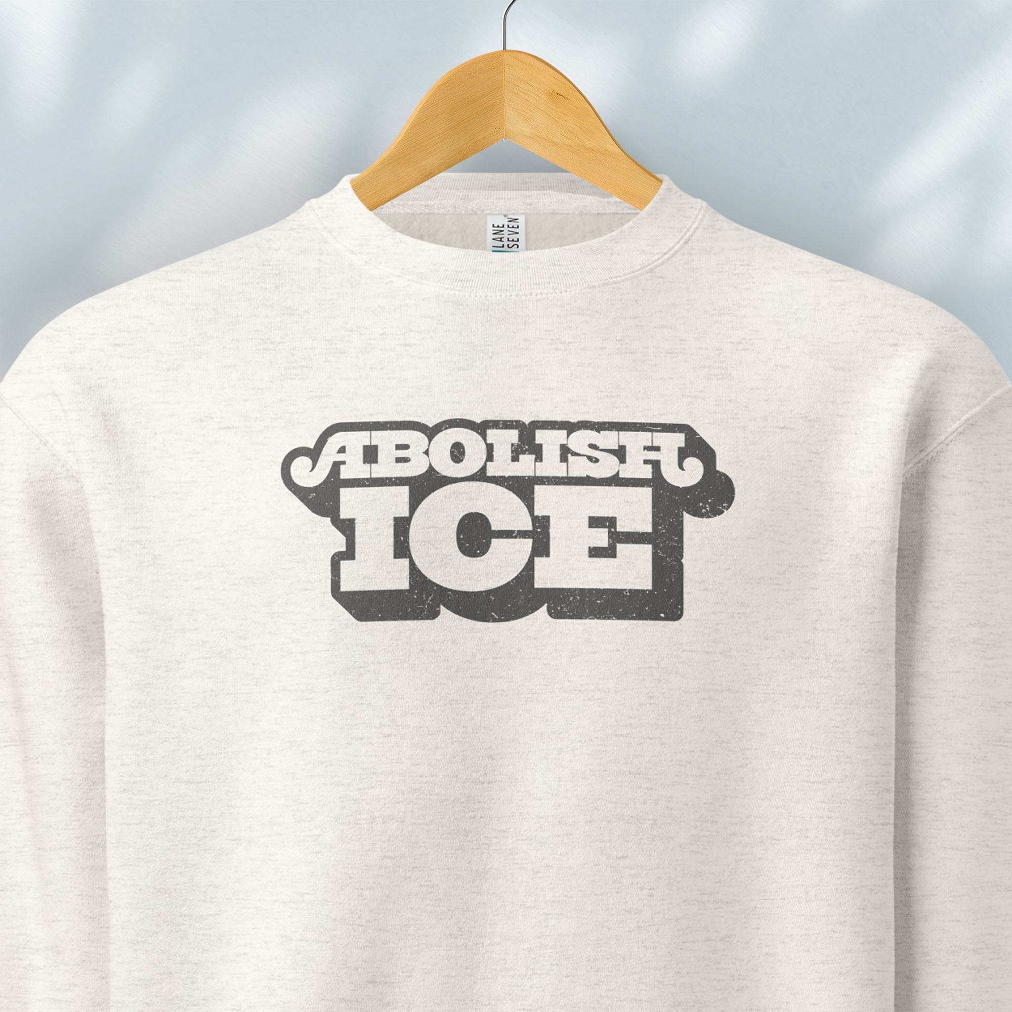 Hanging oatmeal sweatshirt with retro text reading “Abolish ICE” for immigration justice and anti-ICE activism.