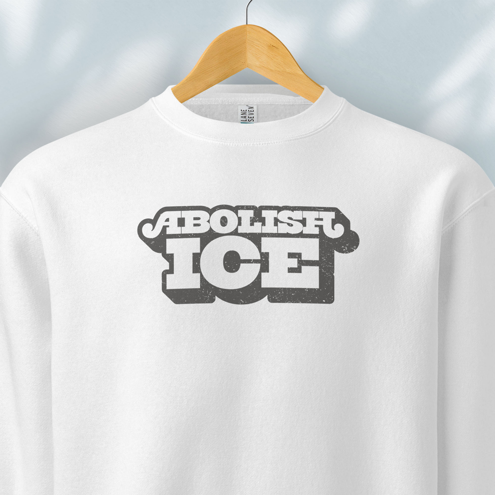 Hanging white sweatshirt with retro text reading “Abolish ICE” for immigration justice and anti-ICE activism.