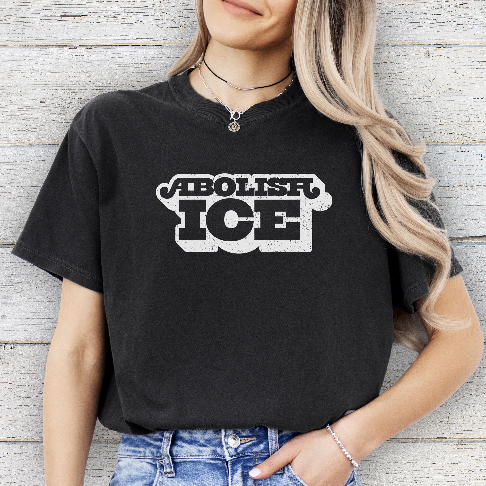 Female model wearing black t-shirt with retro text reading “Abolish ICE” for immigration justice and anti-ICE activism.