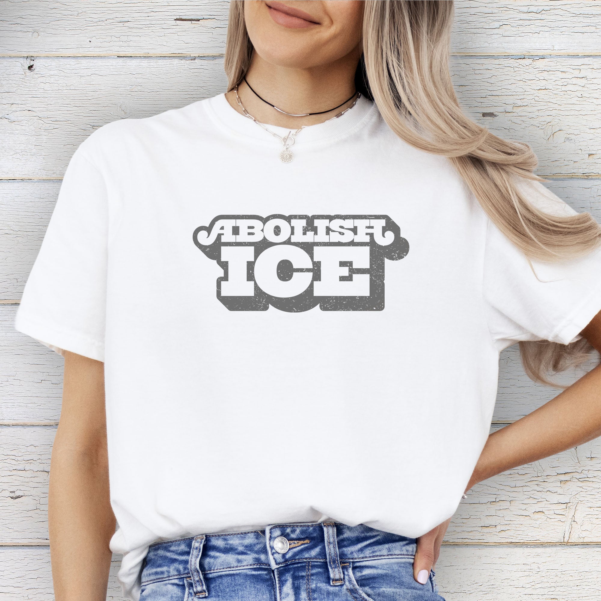 Female model wearing white t-shirt with retro text reading “Abolish ICE” for immigration justice and anti-ICE activism.