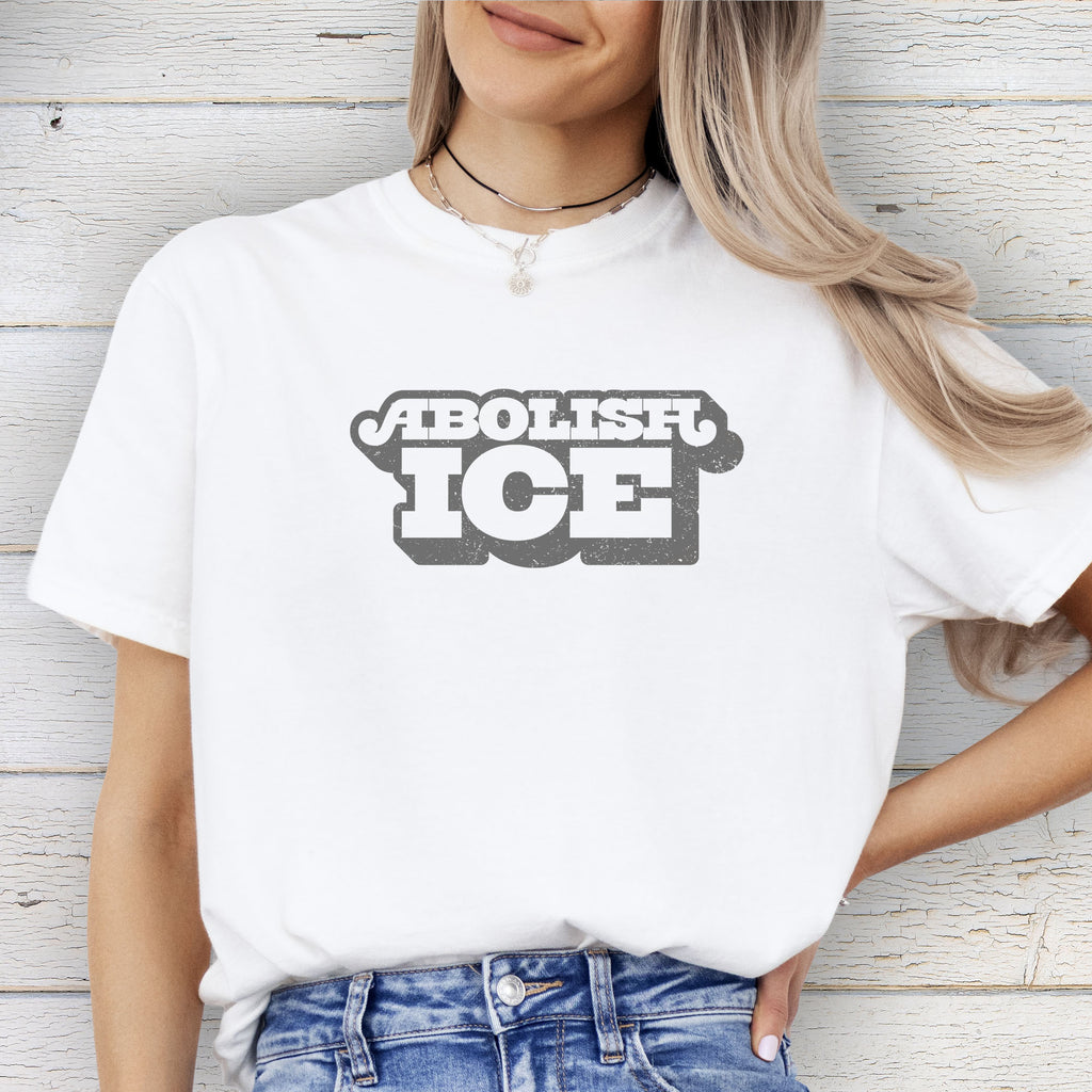 Female model wearing white t-shirt with retro text reading “Abolish ICE” for immigration justice and anti-ICE activism.