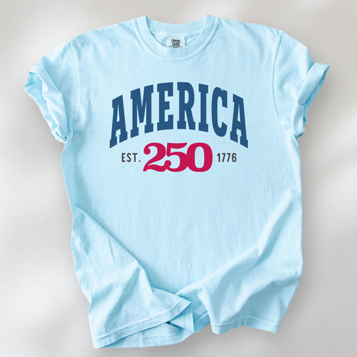 Chambray t-shirt with bold varsity text reading “America 250 — Est. 1776” in varsity style design. 