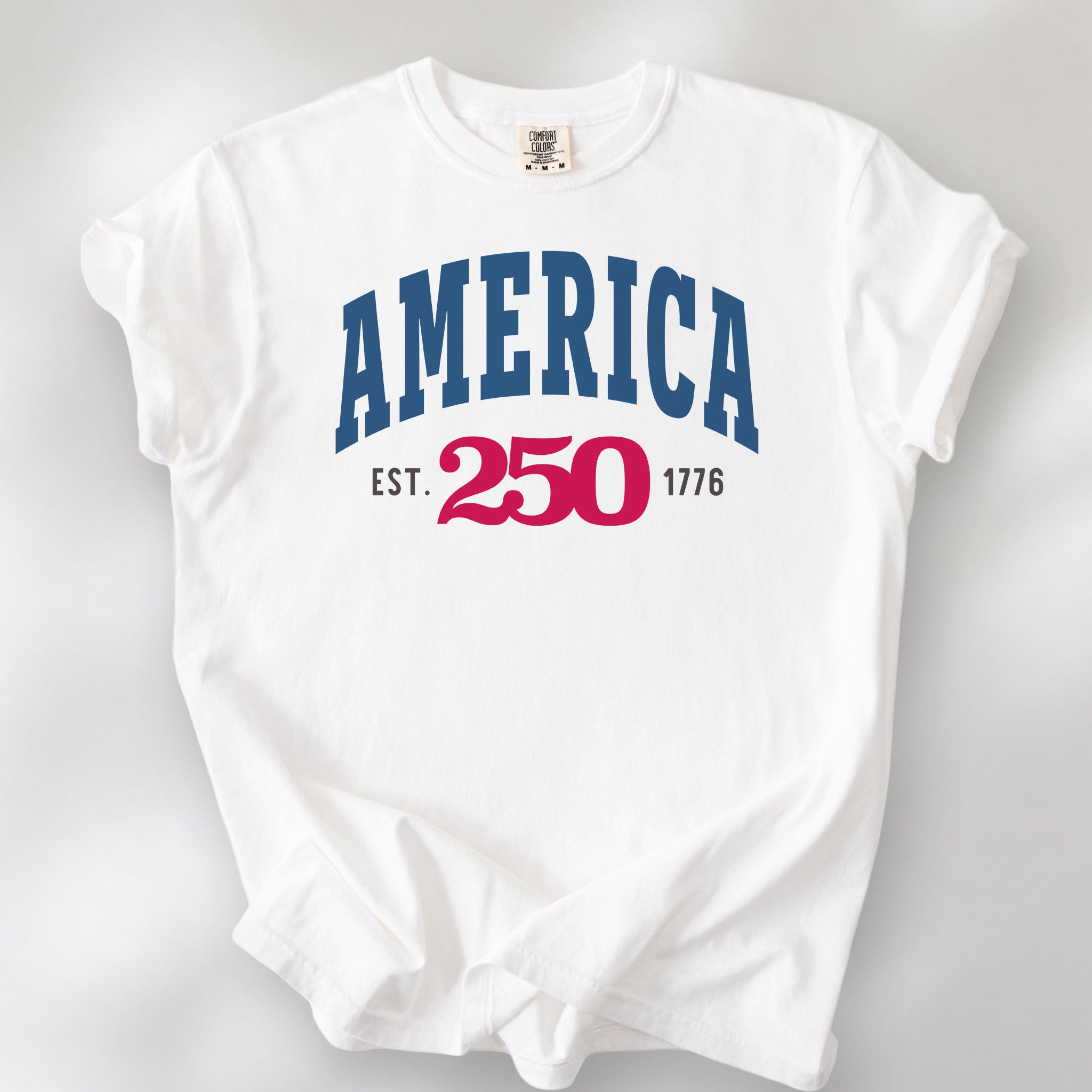 White t-shirt with bold varsity text reading “America 250 — Est. 1776” in varsity style design. 