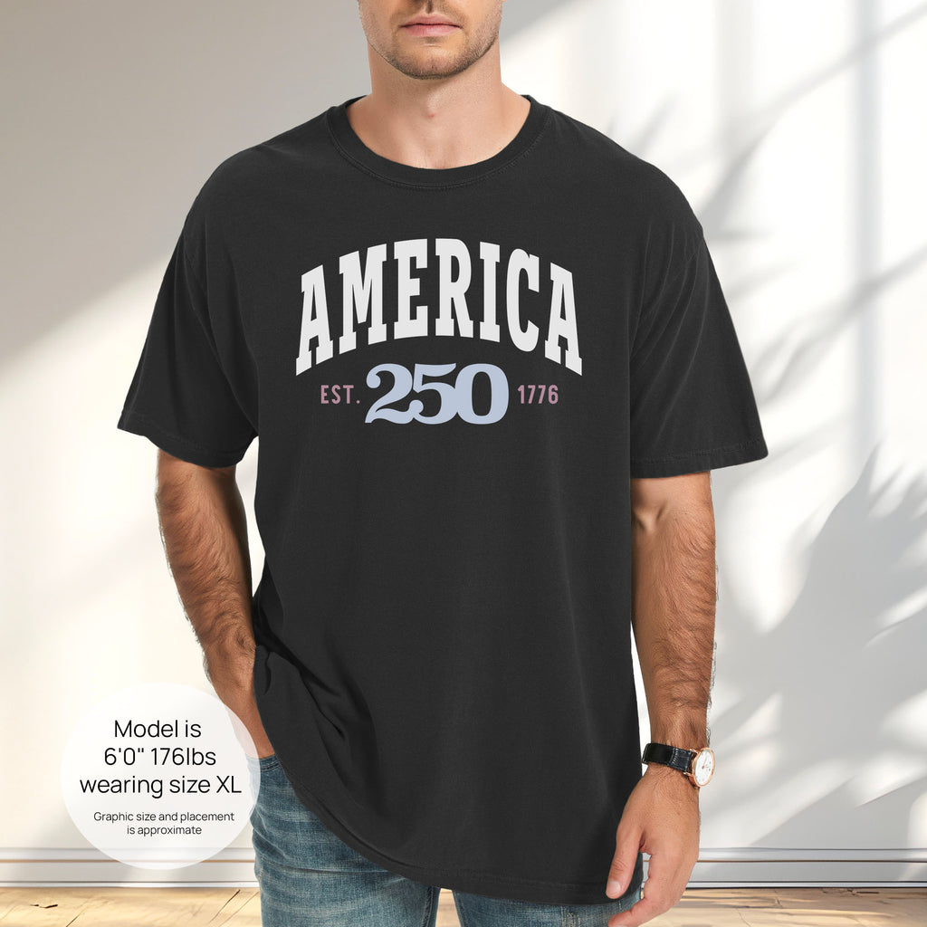 Male model wearing black t-shirt with bold varsity text reading “America 250 — Est. 1776” in varsity style design. Includes size and fit information for the model who is 6 feet 0 inches, 176 pounds, and wearing a size XL shirt.
