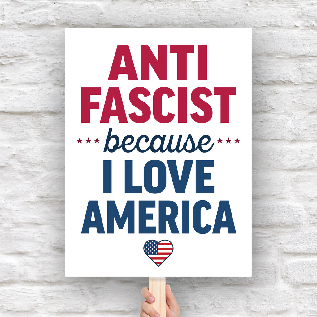 Downloadable, printable protest sign reading “Anti-Fascist Because I Love America” in red and blue lettering with patriotic heart design, anti-Trump rally poster.