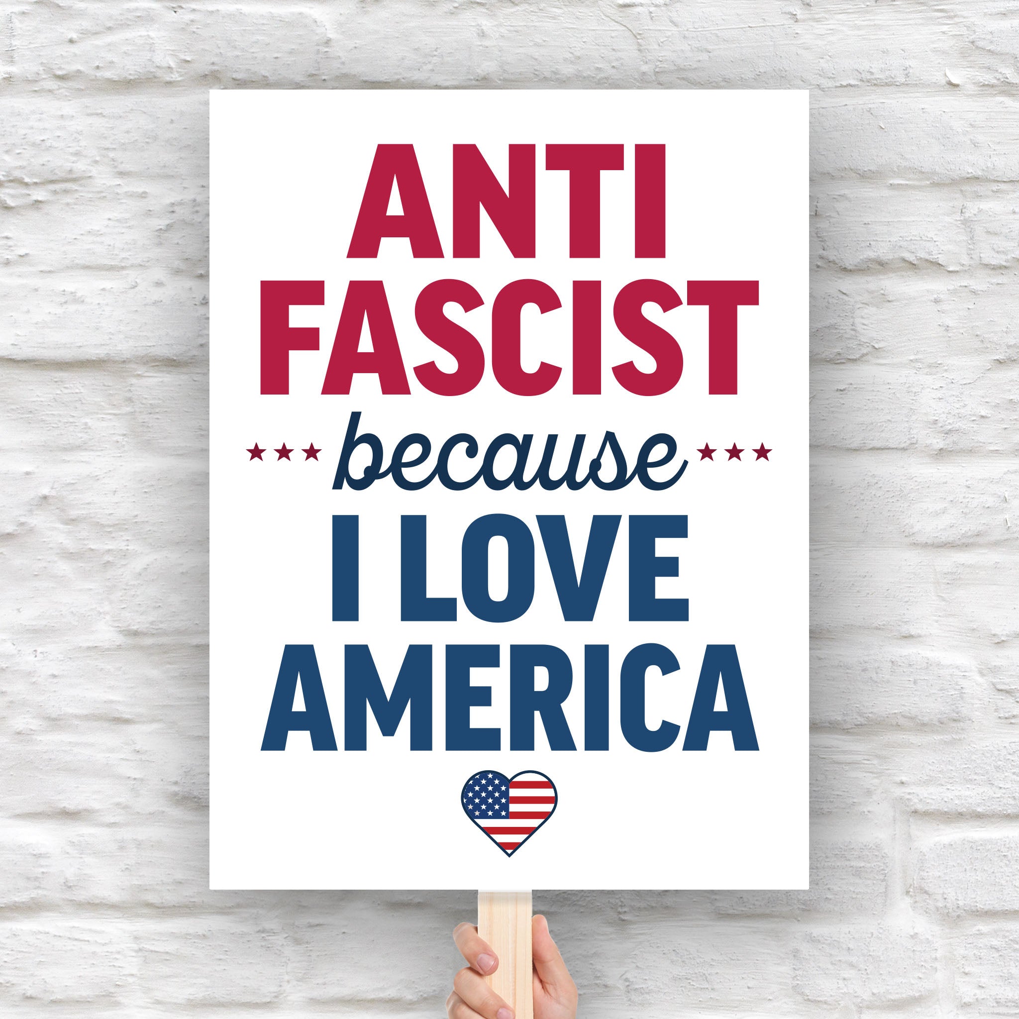 Downloadable, printable protest sign reading “Anti-Fascist Because I Love America” in red and blue lettering with patriotic heart design, anti-Trump rally poster.