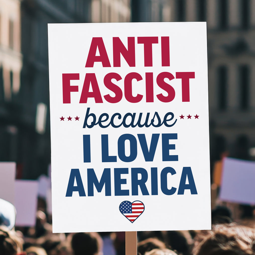 Protest sign reading “Anti-Fascist Because I Love America” in red and blue lettering with patriotic heart design, anti-Trump rally poster, held high above a crowd.