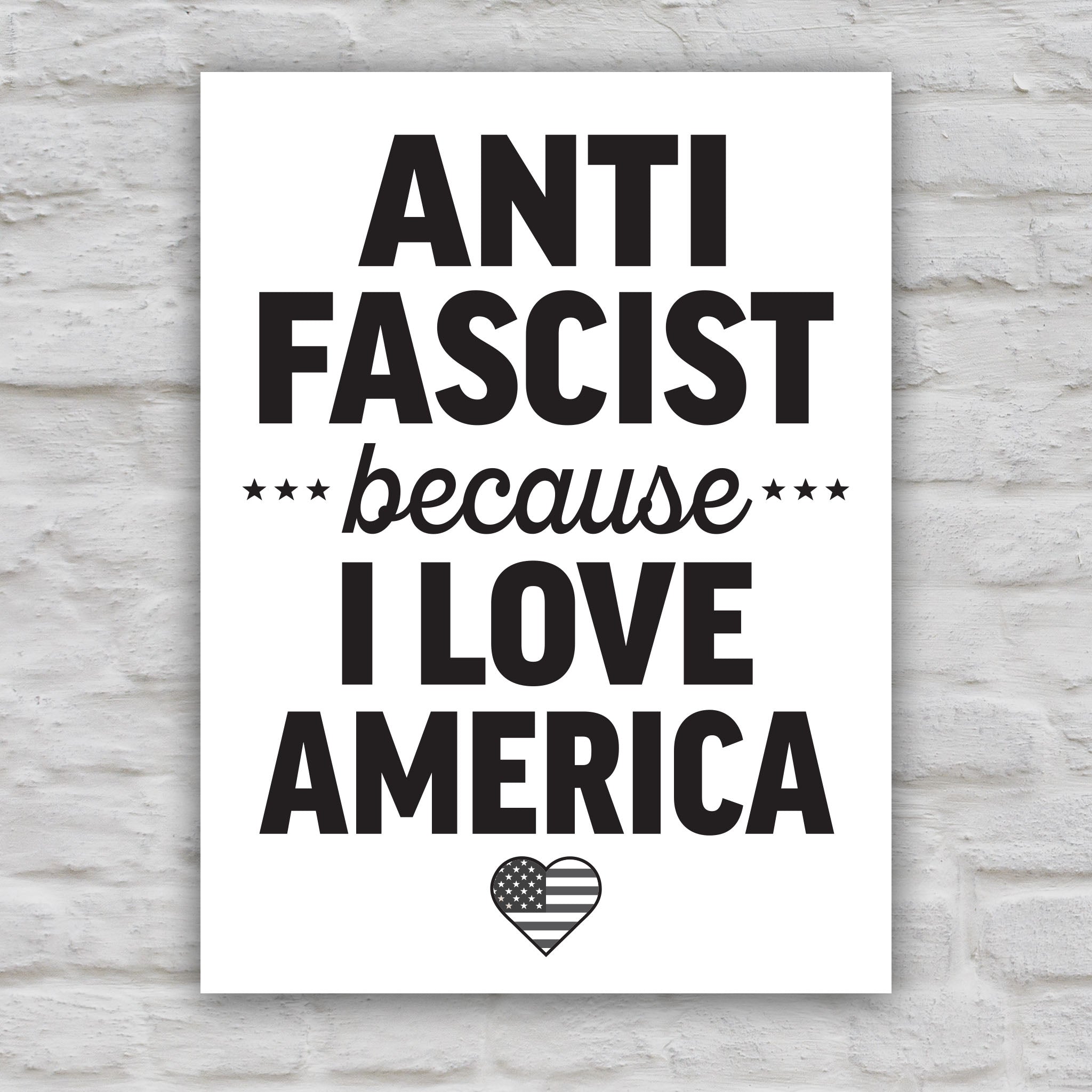 Black and white version of protest sign reading “Anti-Fascist Because I Love America” in bold lettering with patriotic heart design, anti-Trump rally poster.