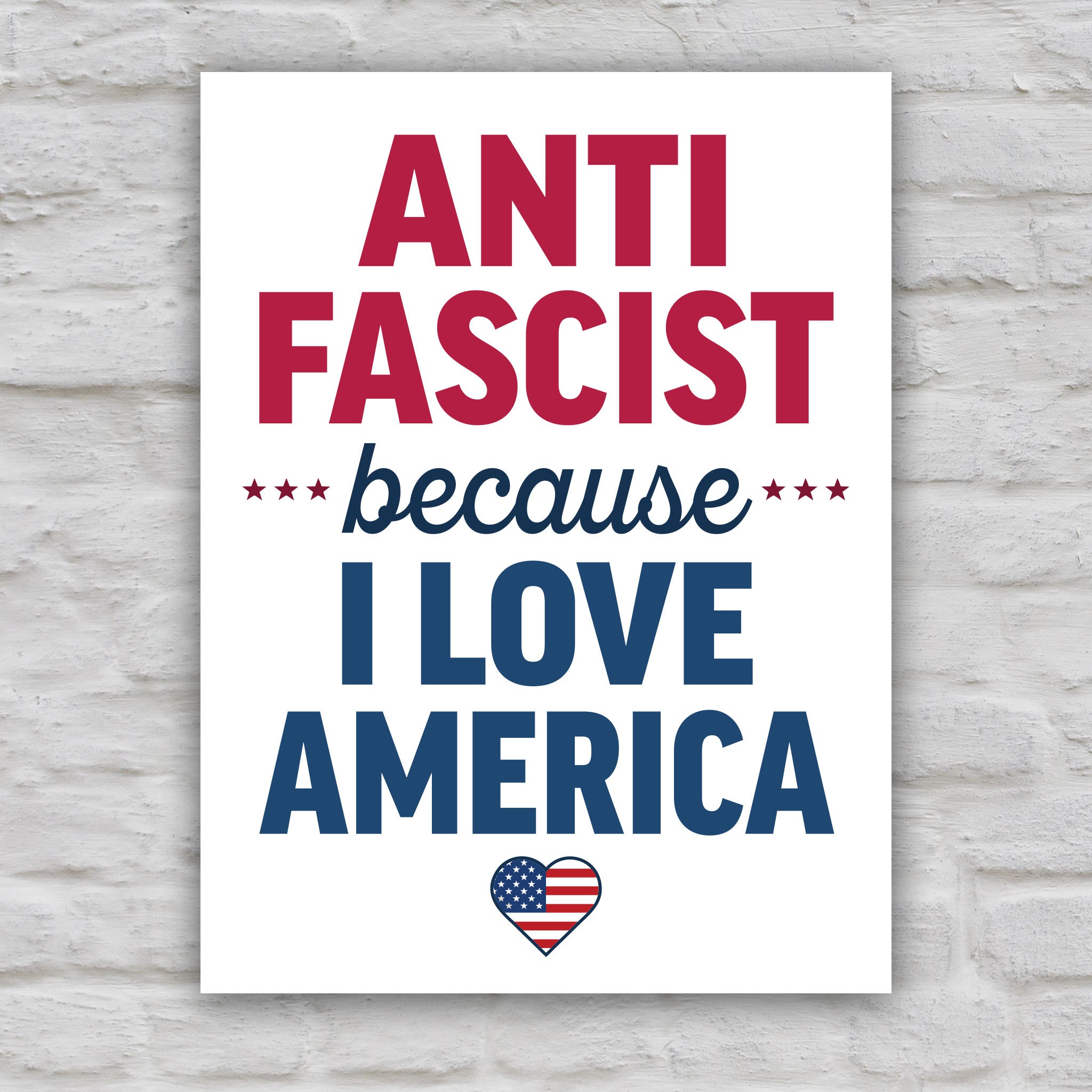 Color version of protest sign reading “Anti-Fascist Because I Love America” in bold lettering with patriotic heart design, anti-Trump rally poster.
