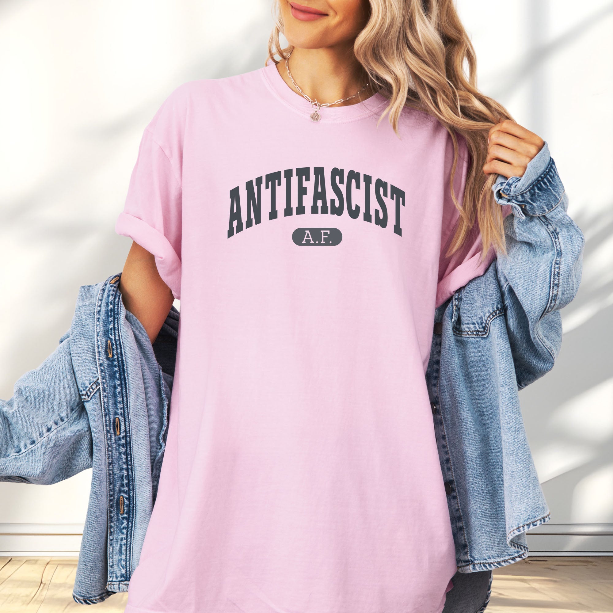 Female model wearing blossom Comfort Colors t-shirt with varsity collegiate style text across the front that reads "Antifascist AF."