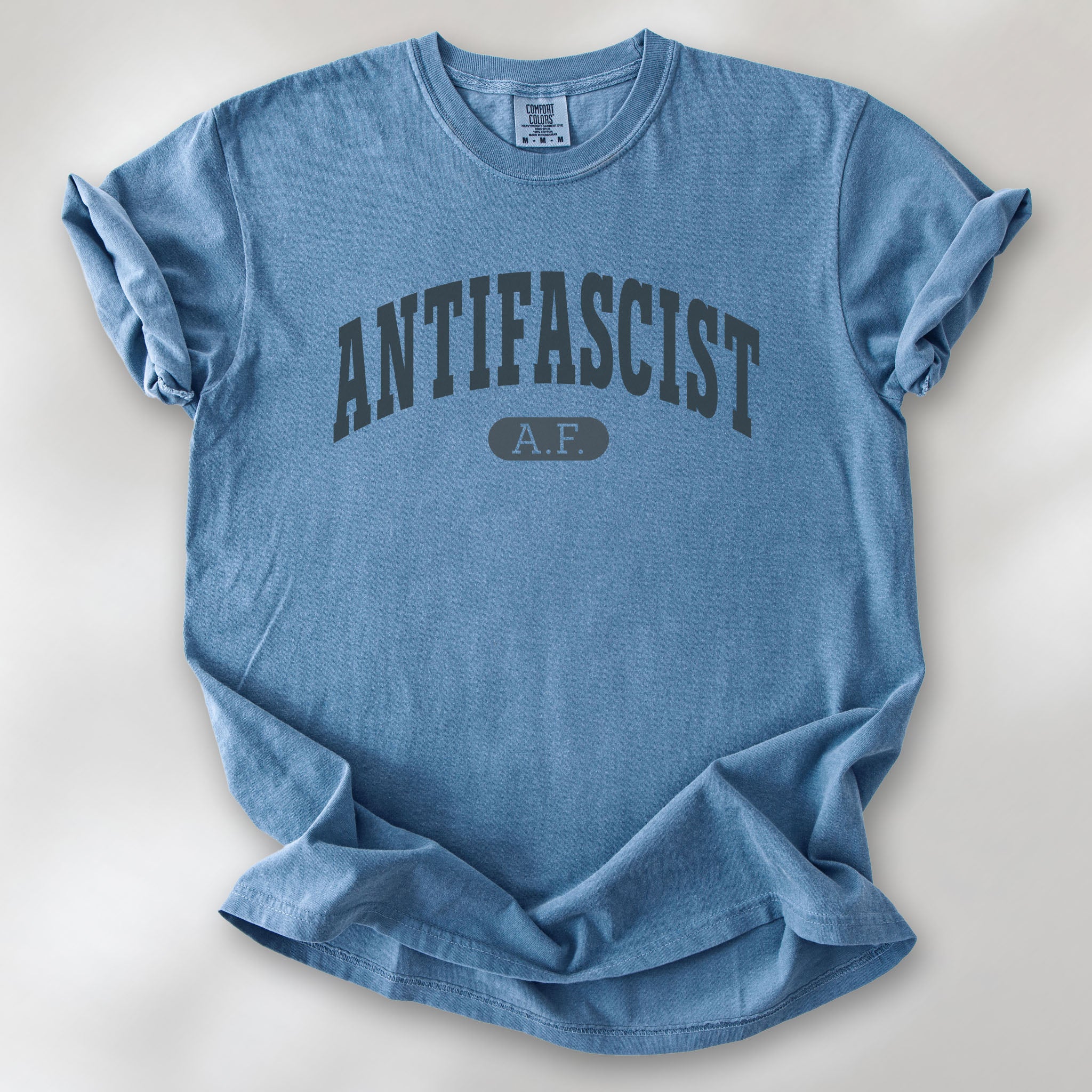 Blue jean Comfort Colors t-shirt with varsity collegiate style text across the front that reads "Antifascist AF."