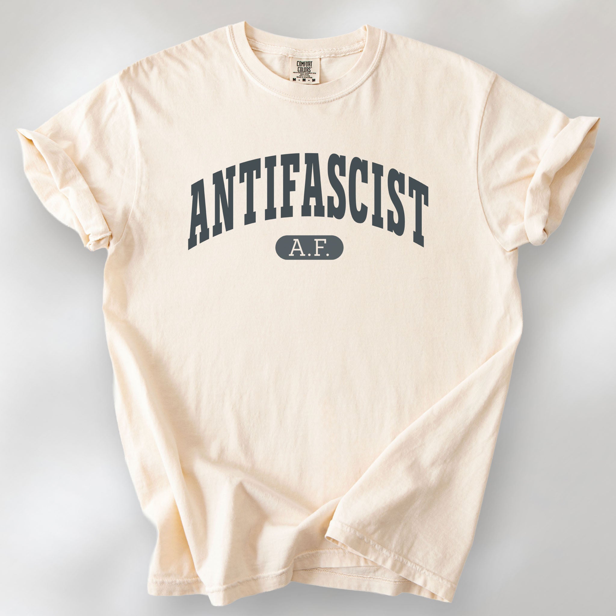 Ivory Comfort Colors t-shirt with varsity collegiate style text across the front that reads "Antifascist AF."
