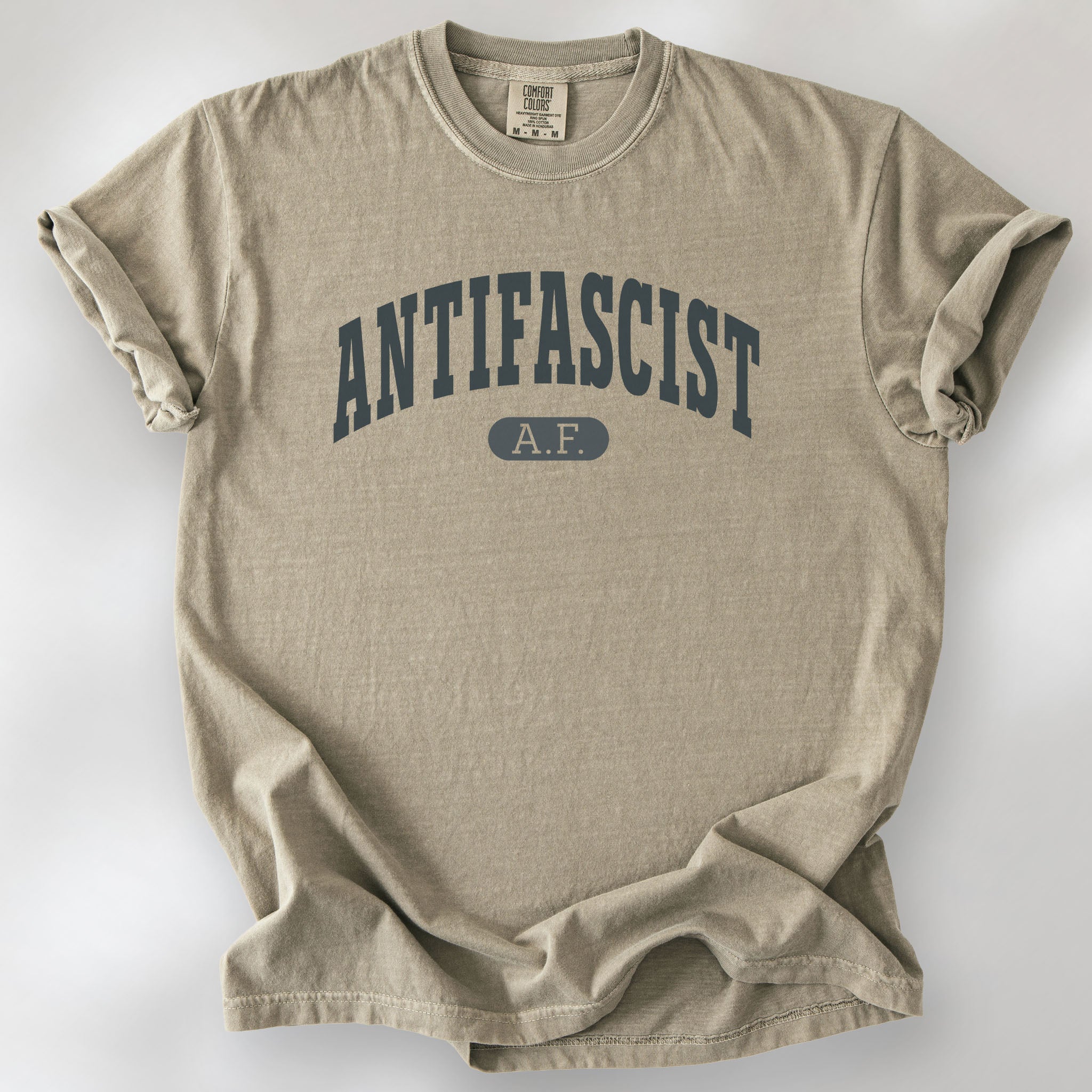 Khaki Comfort Colors t-shirt with varsity collegiate style text across the front that reads "Antifascist AF."