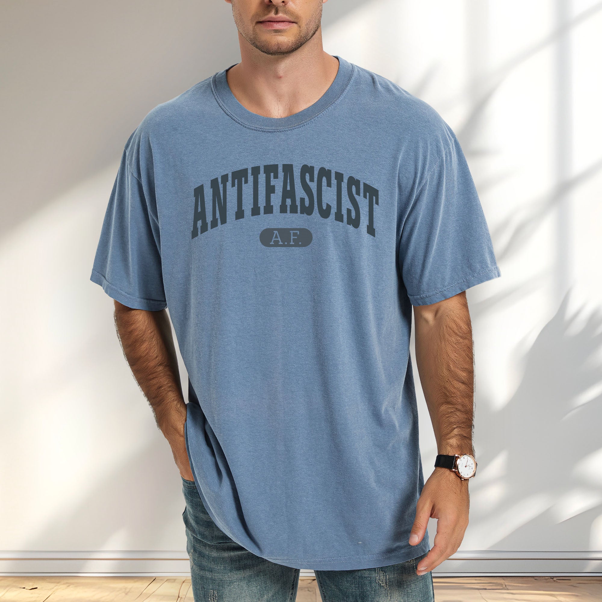 Male model wearing blue jean Comfort Colors t-shirt with varsity collegiate style text across the front that reads "Antifascist AF."