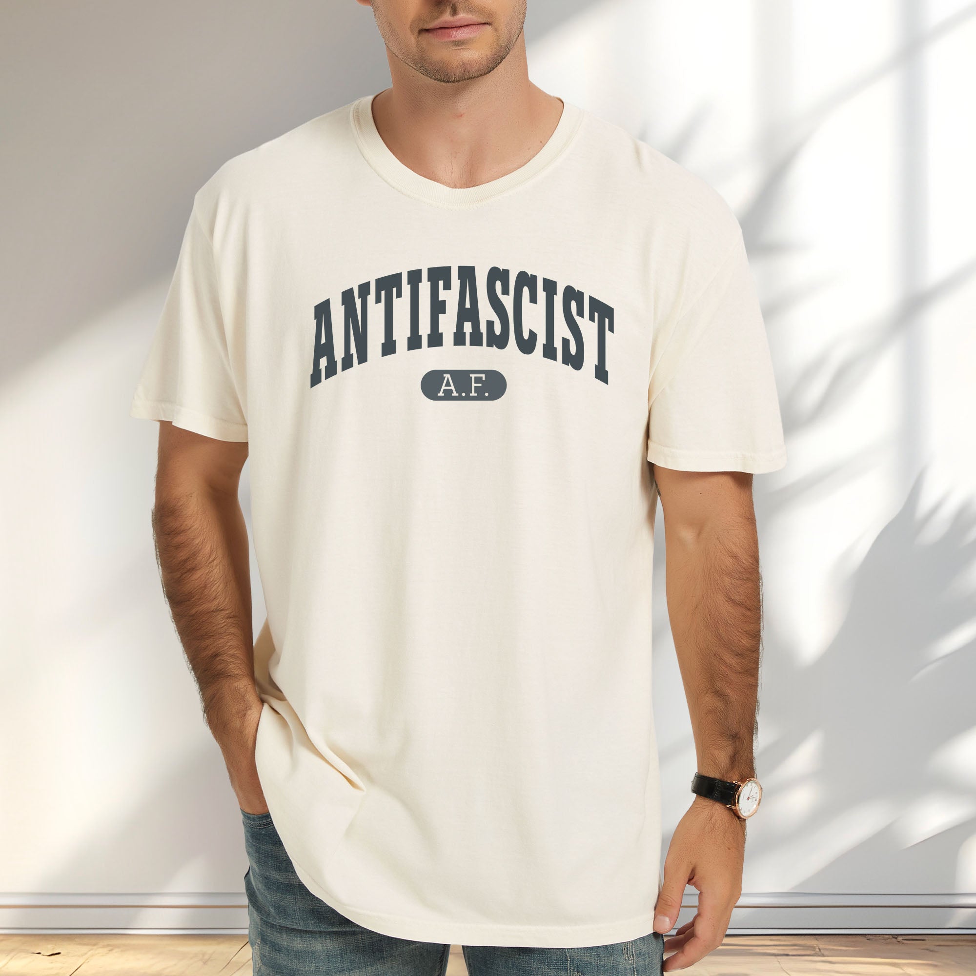 Female model wearing ivory Comfort Colors t-shirt with varsity collegiate style text across the front that reads "Antifascist AF."