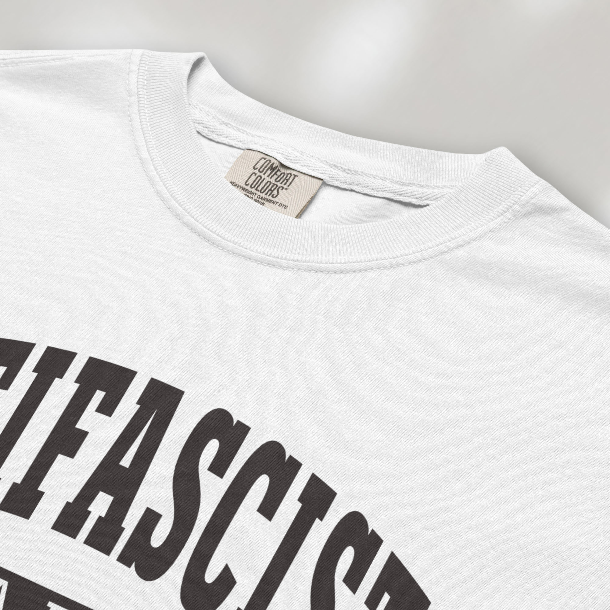 Closeup detail of white Comfort Colors t-shirt with varsity collegiate style text across the front that reads "Antifascist AF."