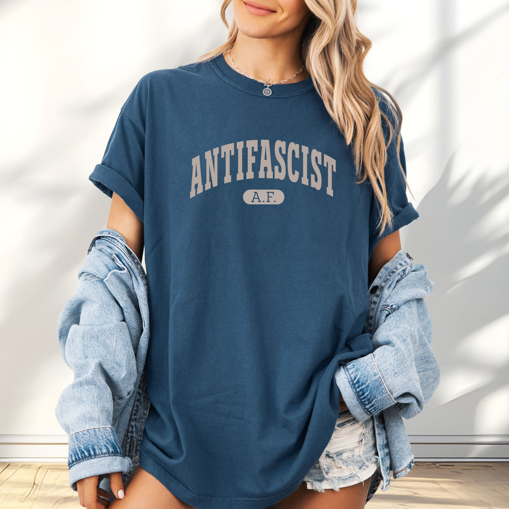 Female model wearing oversized midnight Comfort Colors t-shirt with varsity collegiate style text across the front that reads "Antifascist AF."